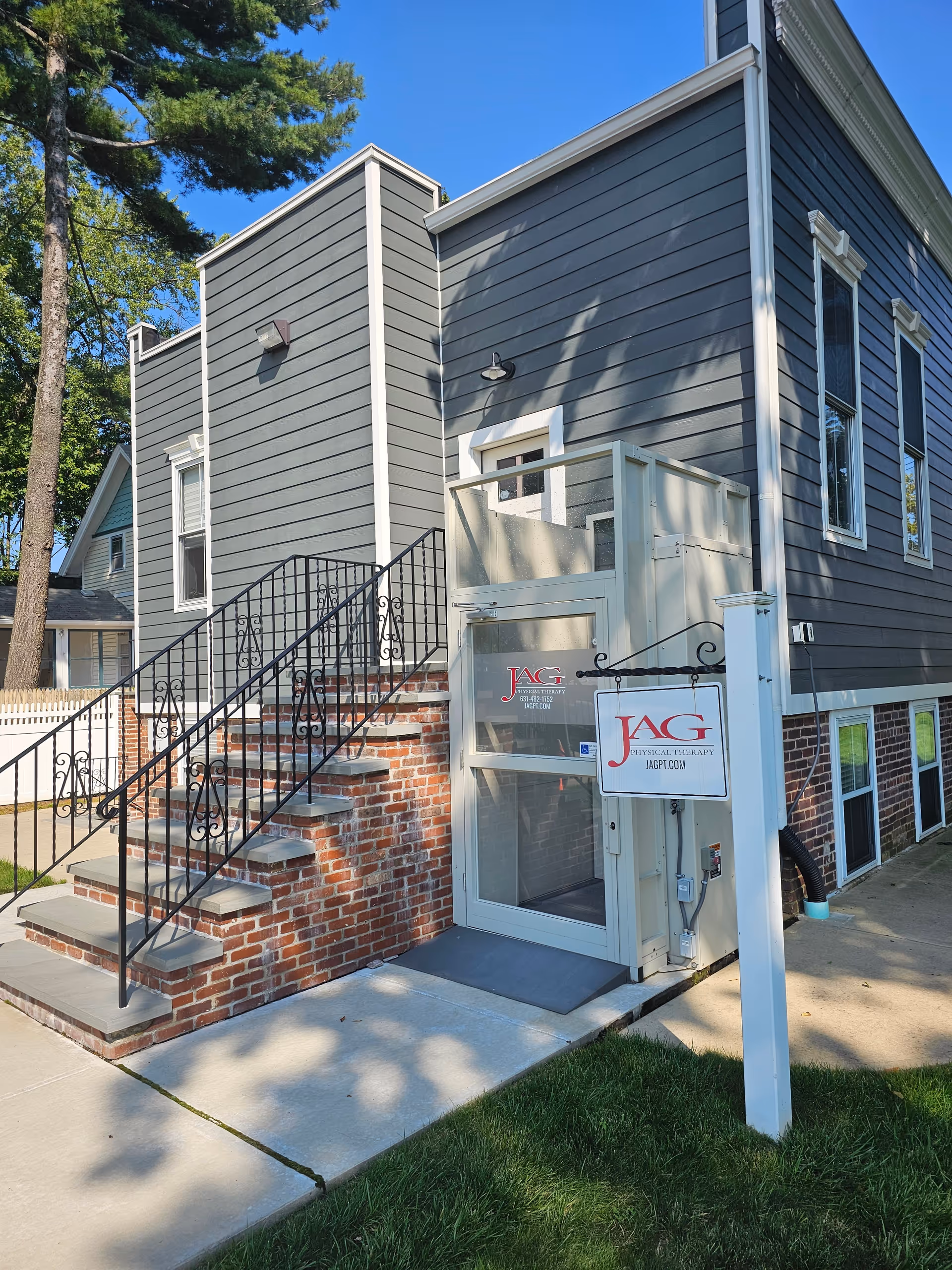 Exterior view of a gray building entrance with brick stairs and a JAG Physical Therapy sign.
