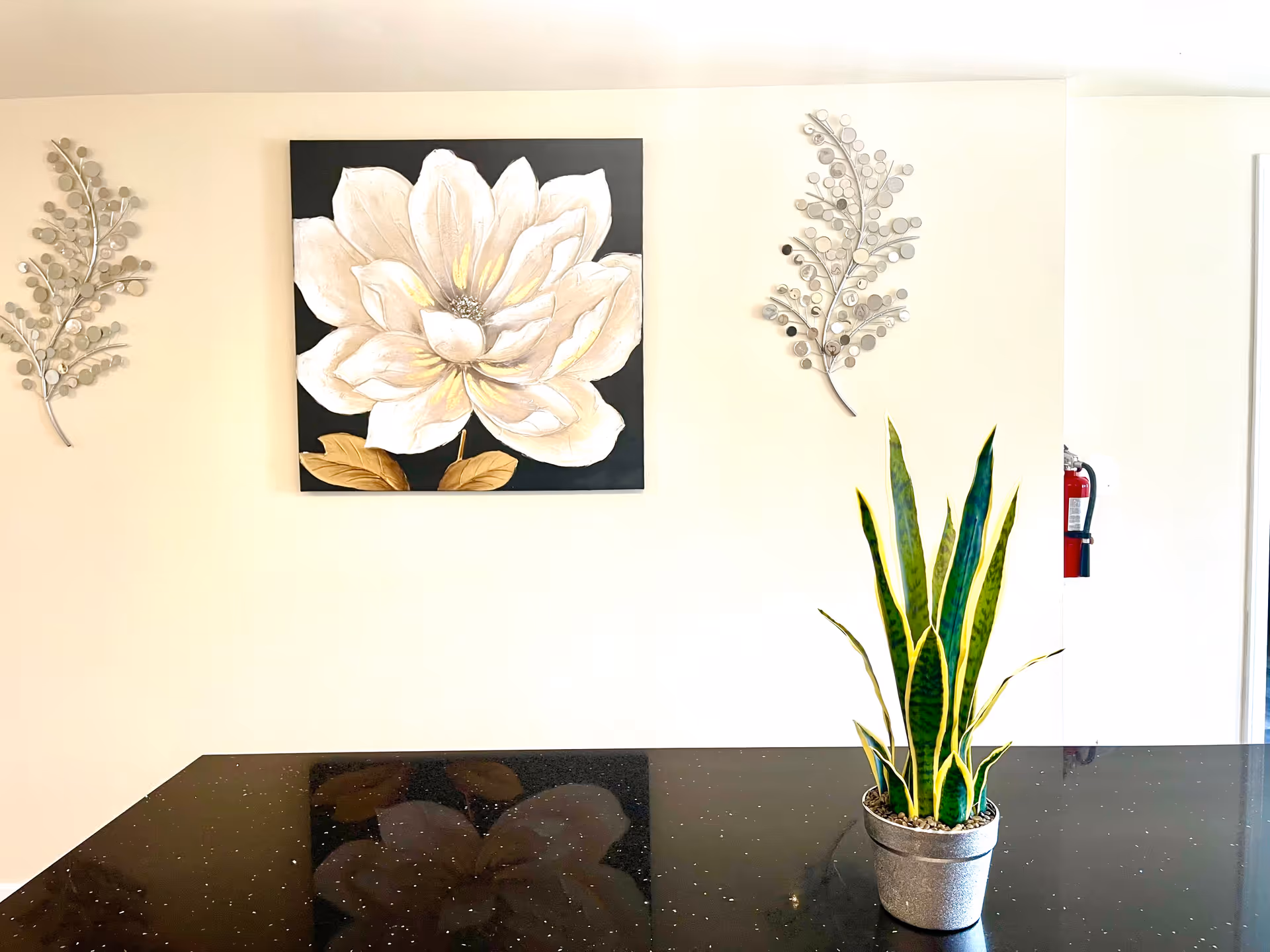 Interior wall features a floral painting, decorative metal branches, and a snake plant on a counter.