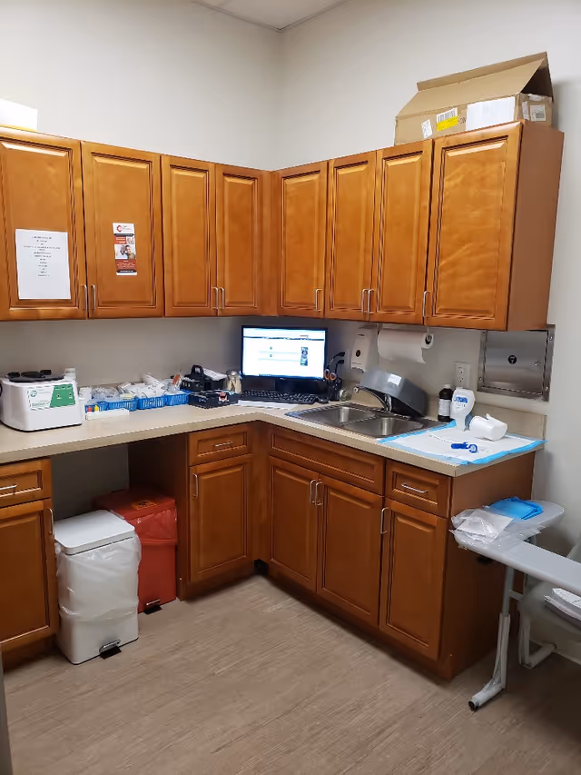 Kitchen area with wooden cabinets, sink, computer monitor, and medical supplies.