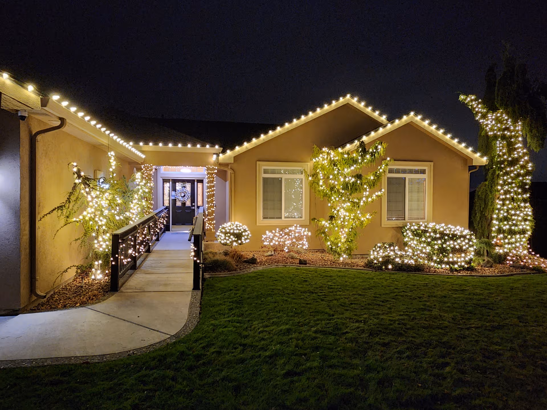 Nighttime exterior of Clovernook Adult Family Home with string lights along roof and shrubs