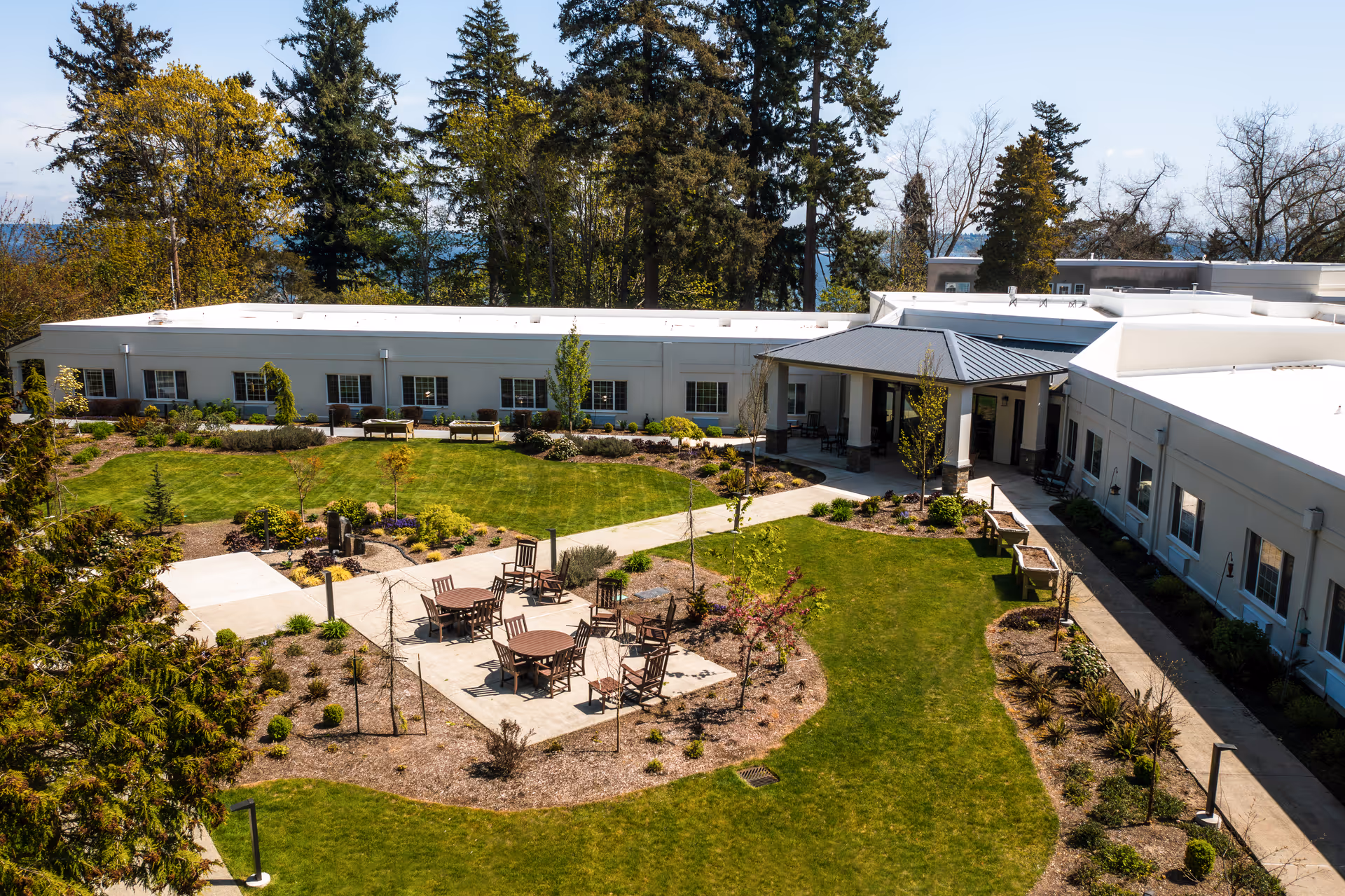 Outdoor courtyard of a senior living facility with tables, chairs, and central entrance.