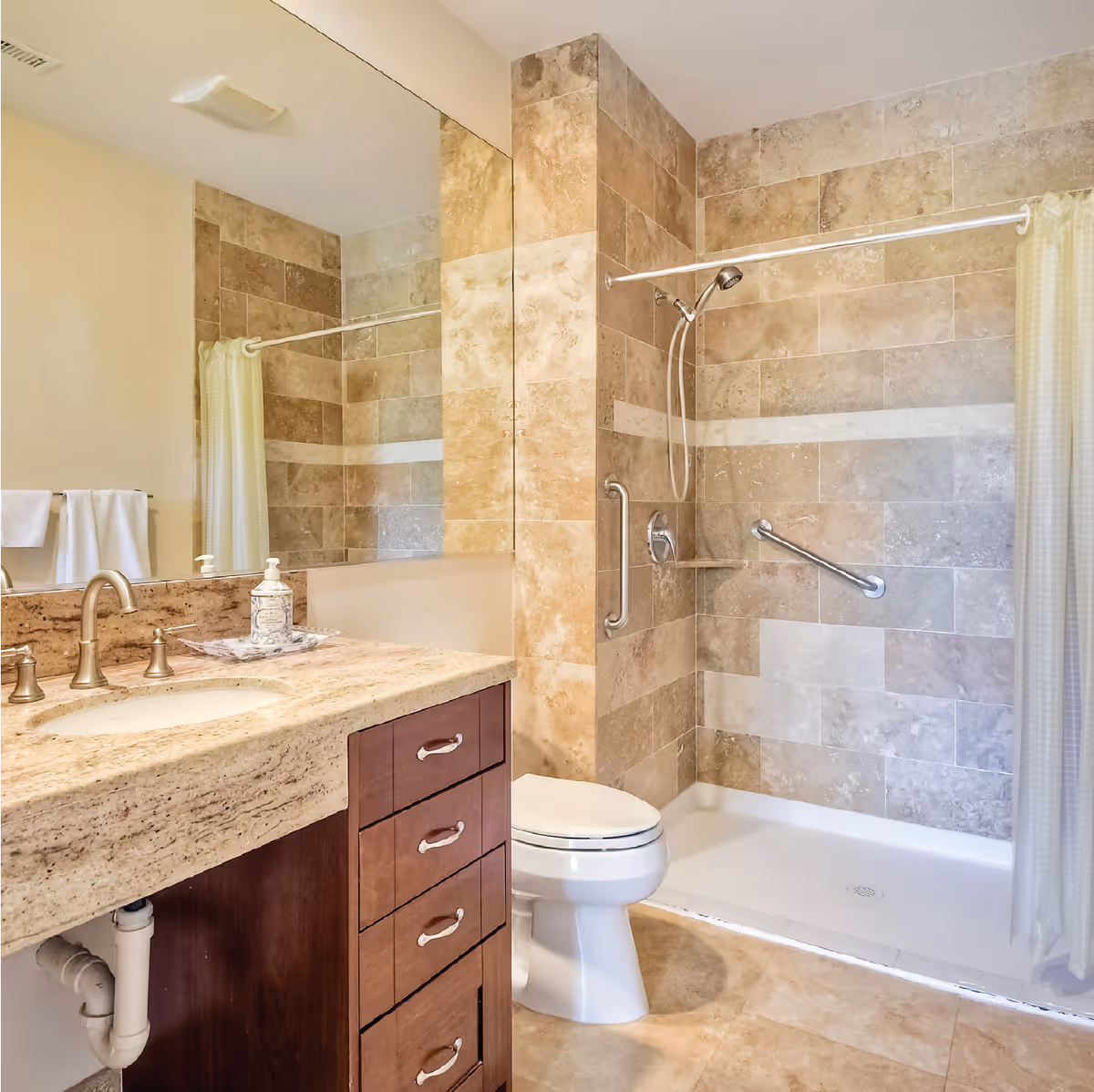 Tiled bathroom featuring a vanity with a stone countertop, toilet, and a walk-in shower with grab bars and a curtain.