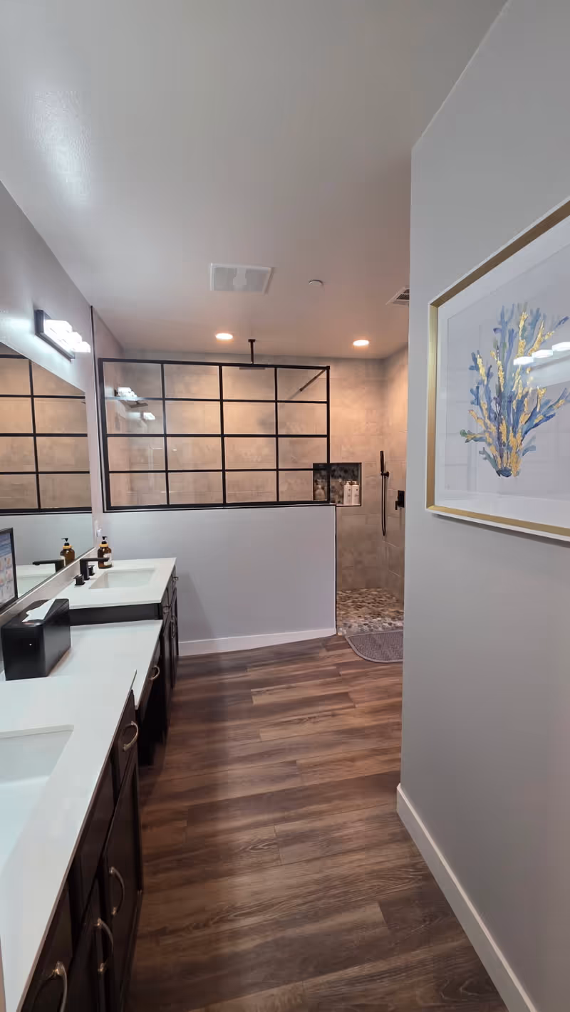 Modern bathroom vanity with double sinks, glass partition, and tiled shower area.