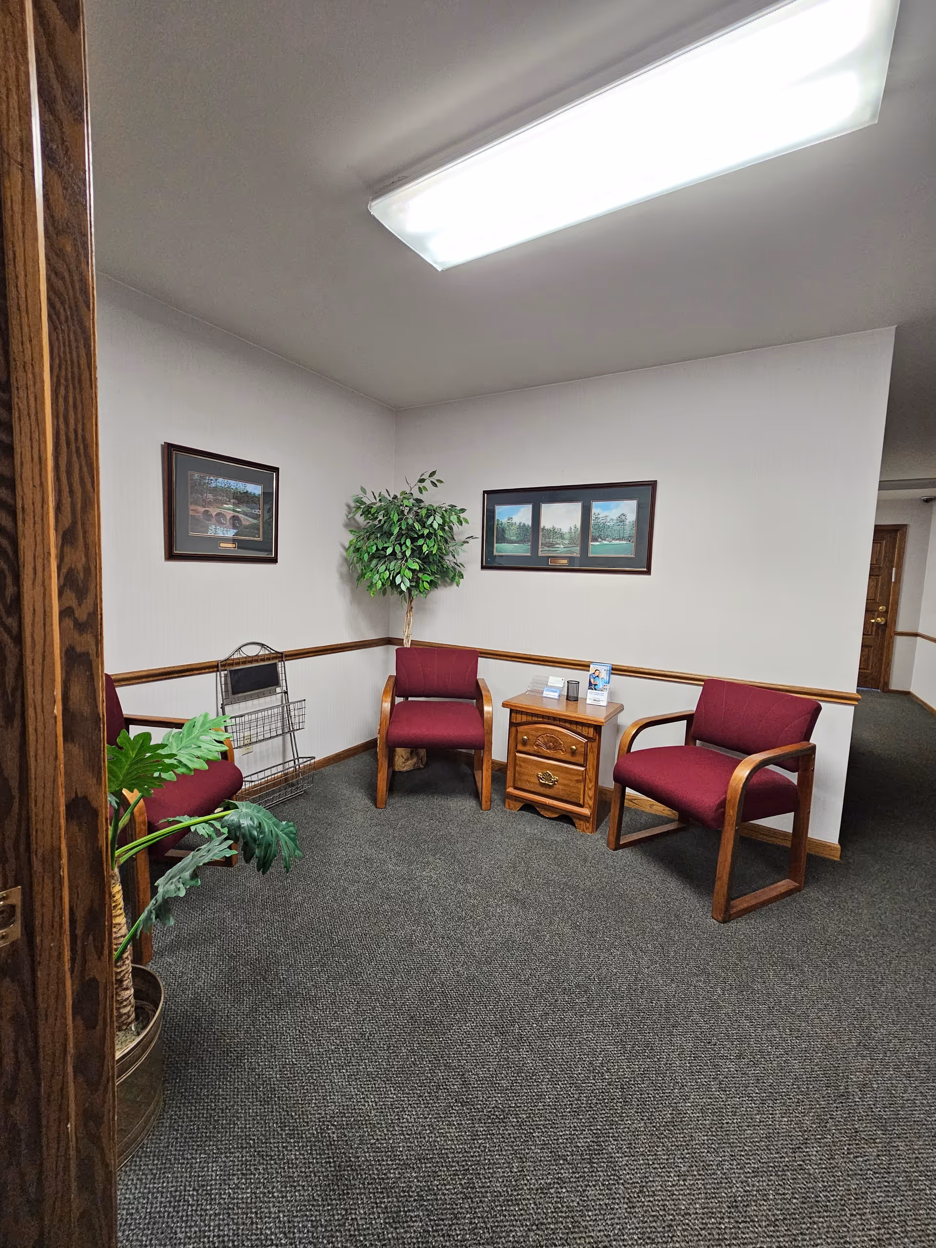 A small waiting area in a senior living facility with burgundy chairs and a wooden table.