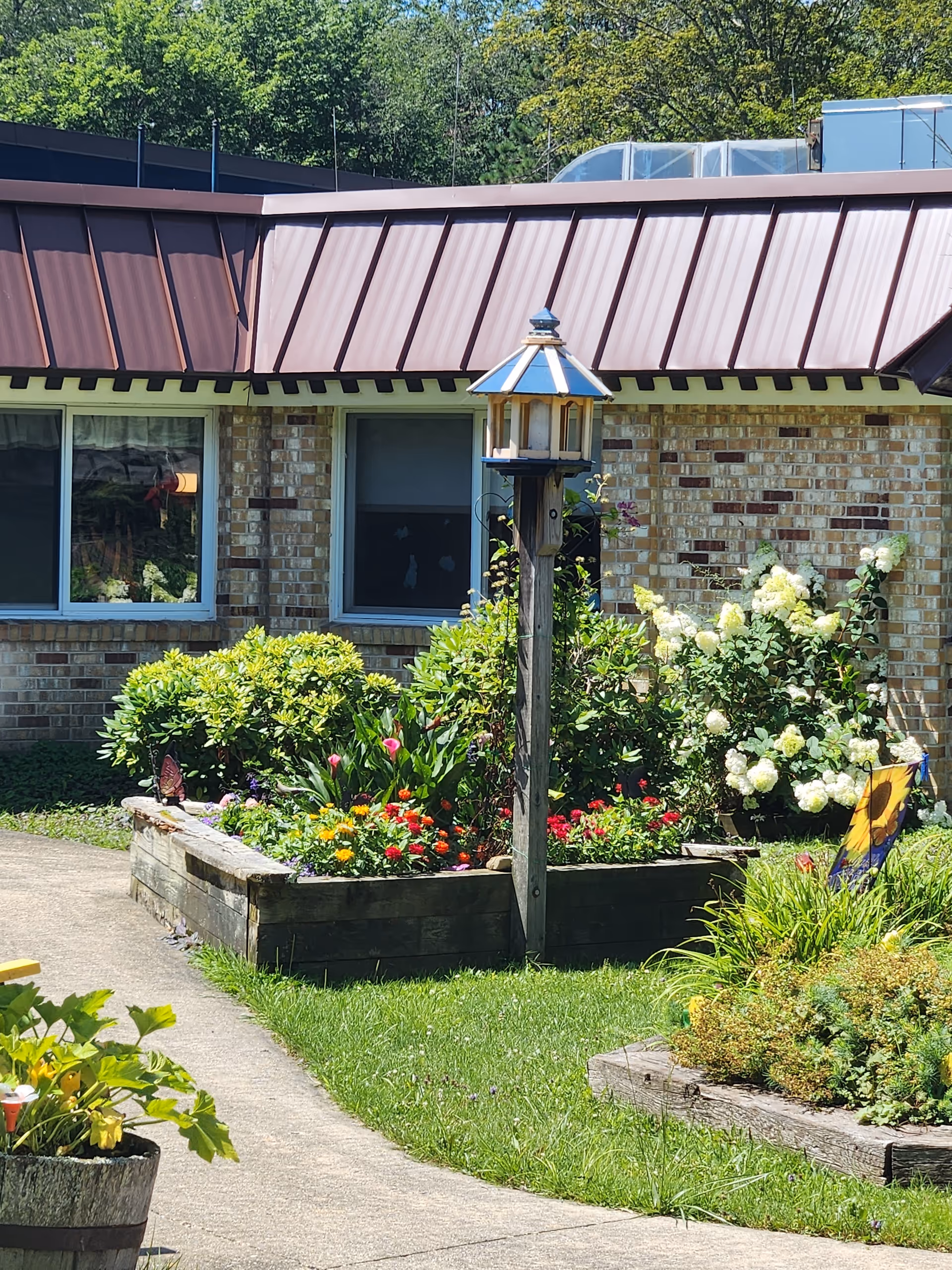Brick nursing home exterior with a colorful garden, raised beds, and a wooden birdhouse.