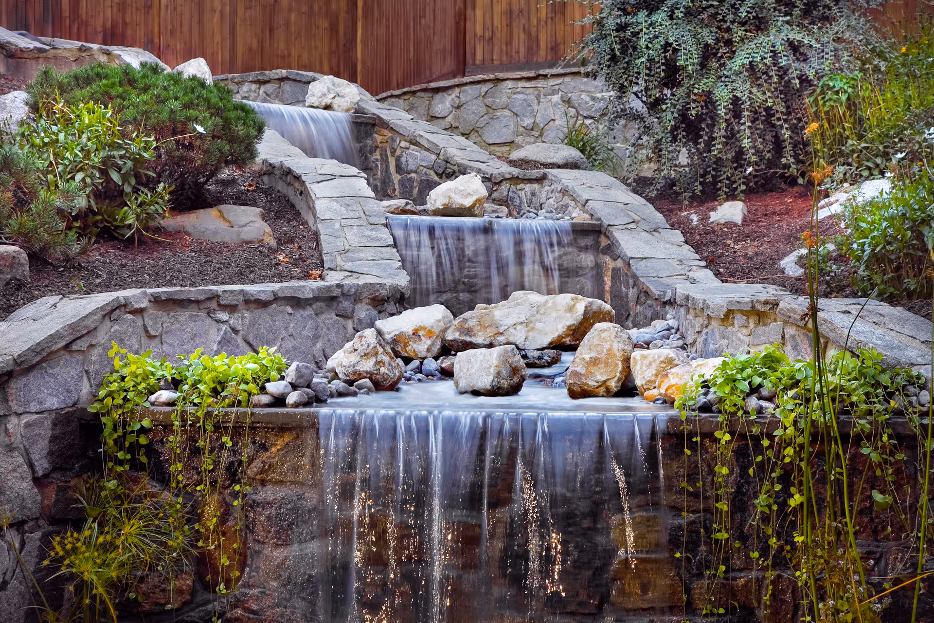 Stone terrace with a cascading outdoor waterfall, rocks, and greenery.