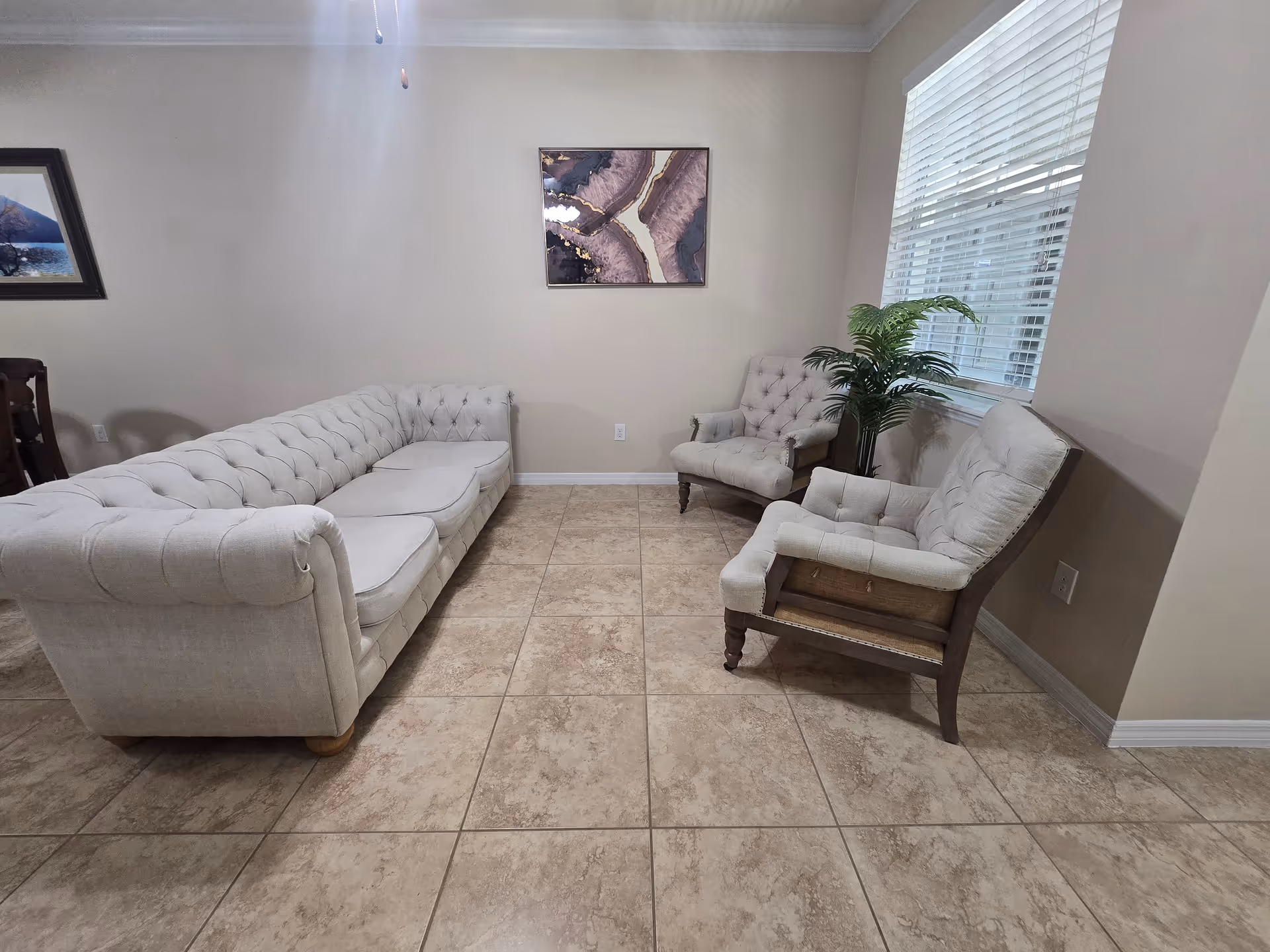 Bright lounge with tufted beige sofa, chairs, and a potted plant by a window.