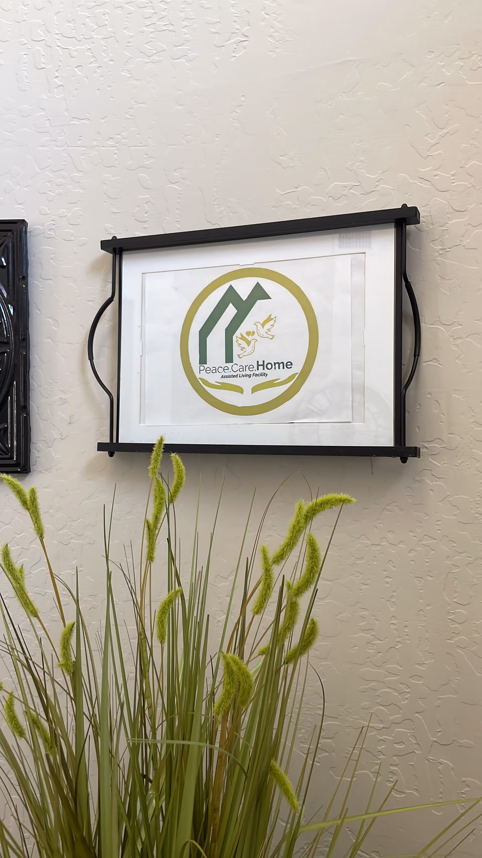 Exterior wall with Peace Care Home sign and ornamental grasses in foreground.