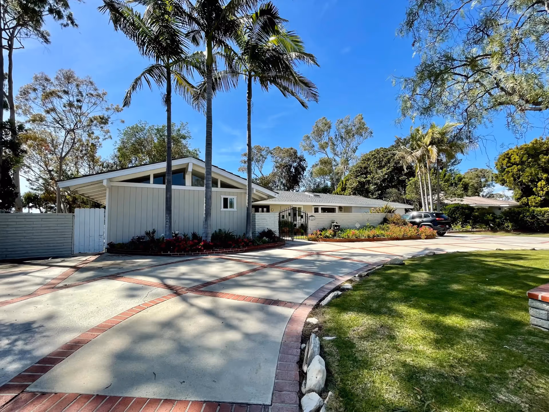 Single-story senior living facility exterior with curved brick pathway, lawn, and palm trees.