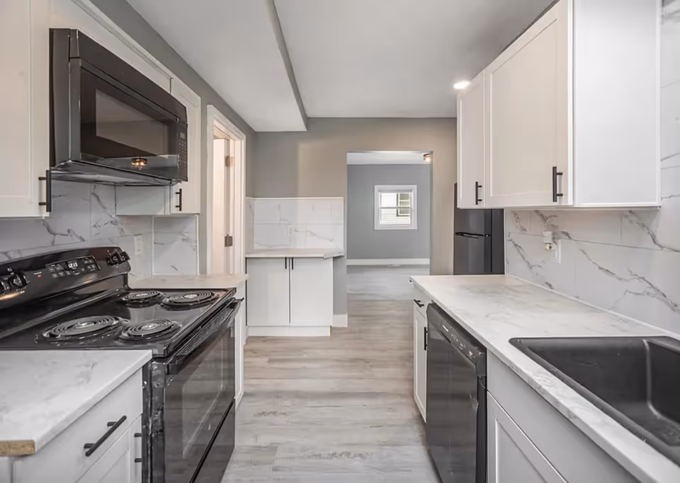 Modern white kitchen with marble countertops, stainless appliances, and gray walls.