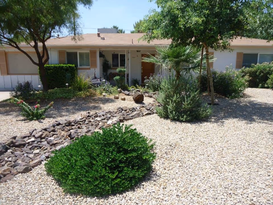 Front exterior of a single-story ranch-style building with a gravel xeriscaped yard, shrubs, and small trees.