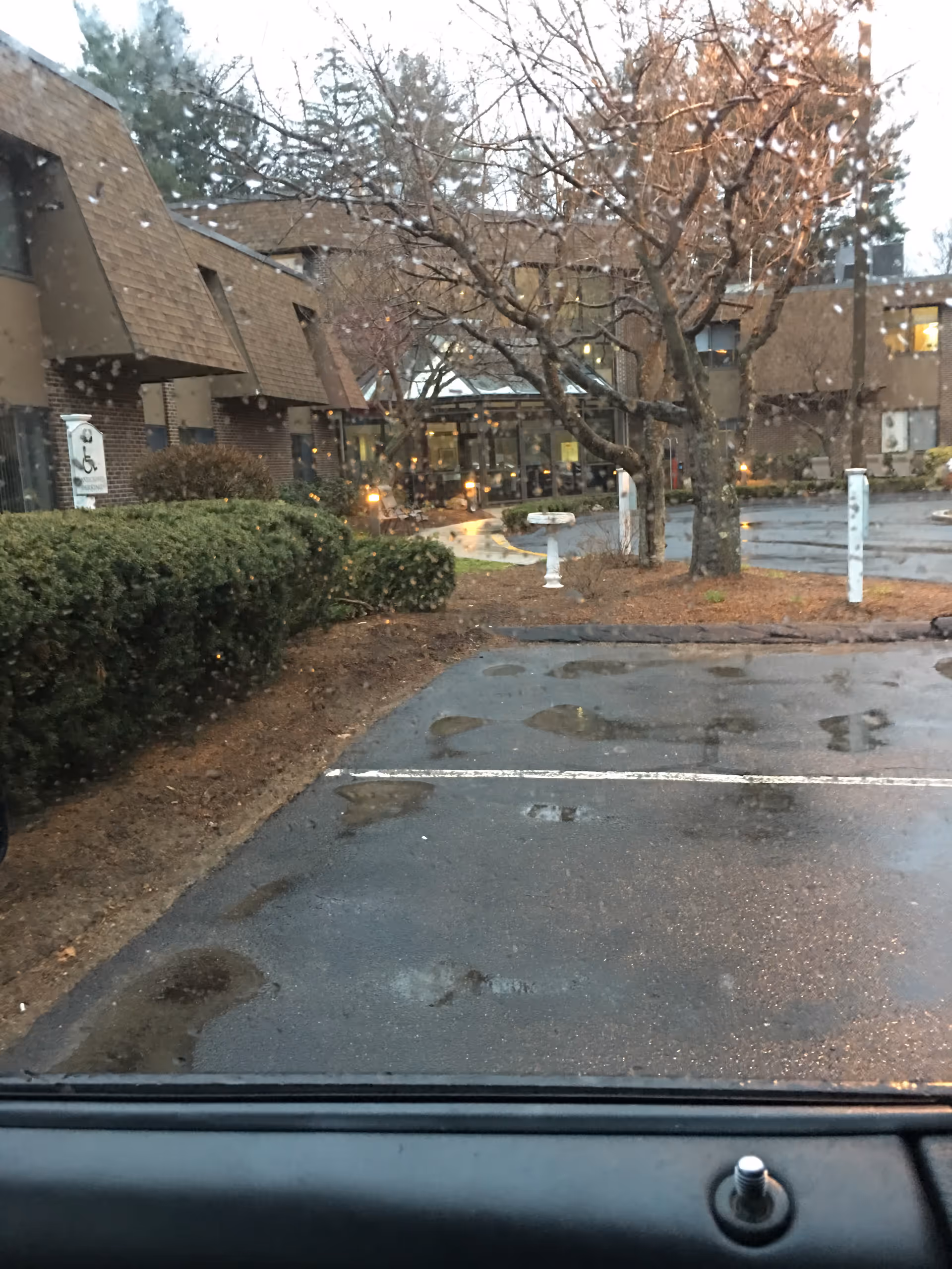 Wet parking lot and snow flurries in front of Vantage Health and Rehab of Wilbraham entrance