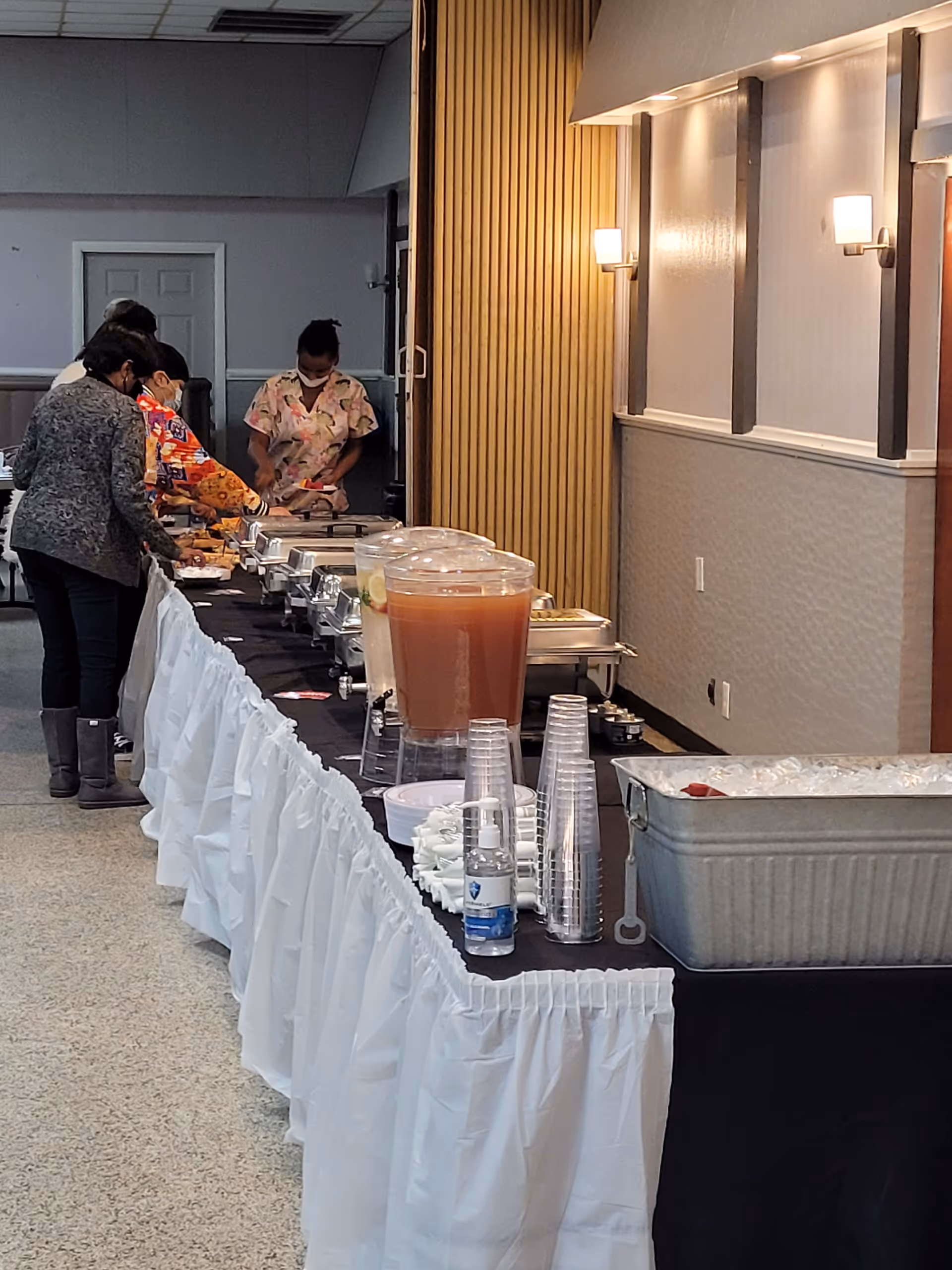 Buffet line along a long table with chafing dishes and staff serving residents.