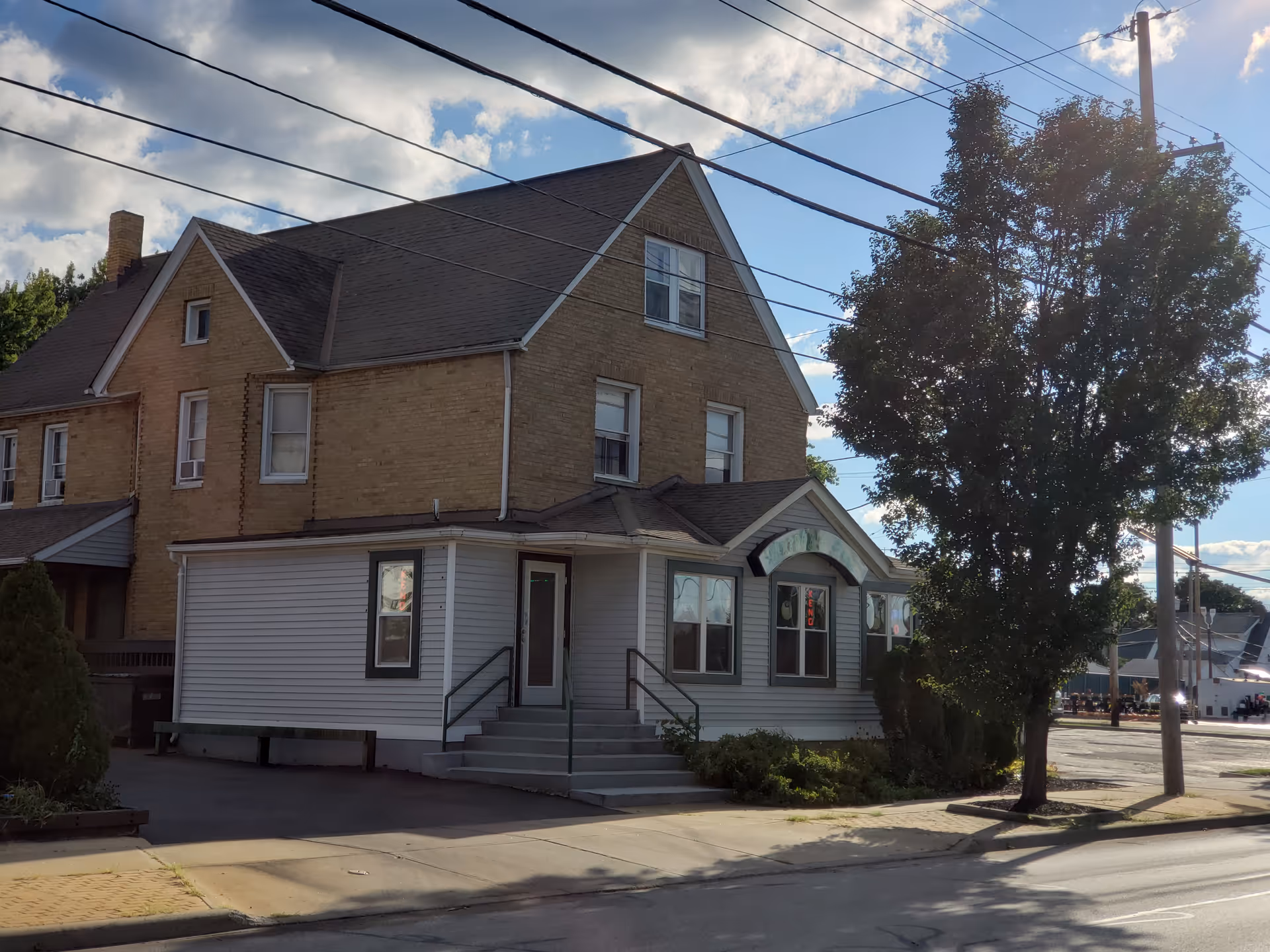 Two-story brick building with a light-gray storefront annex along a sunny street.