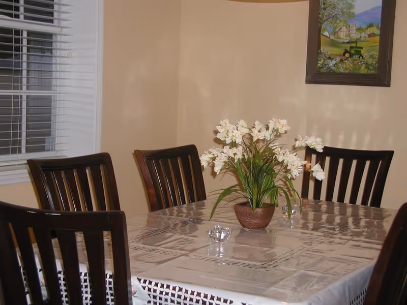 Dining room with a wooden table, chairs, a flower centerpiece, and a wall painting.