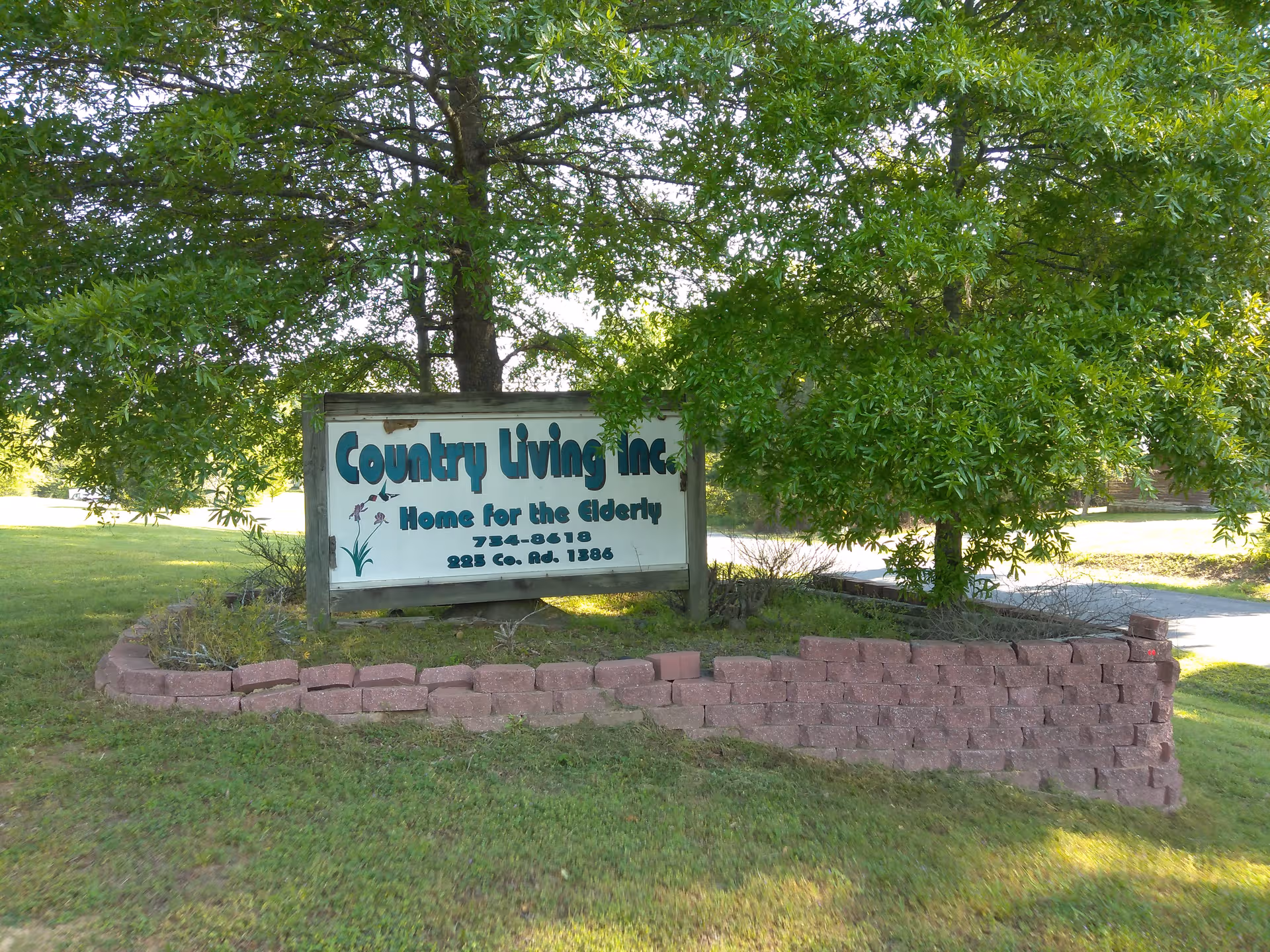Free-standing sign for Country Living Inc. surrounded by trees and a brick border.