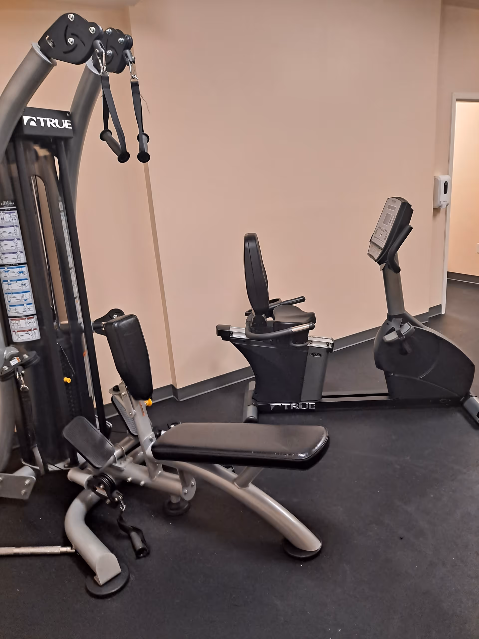 Indoor gym area with weight machines and a stationary bike in a senior living facility.
