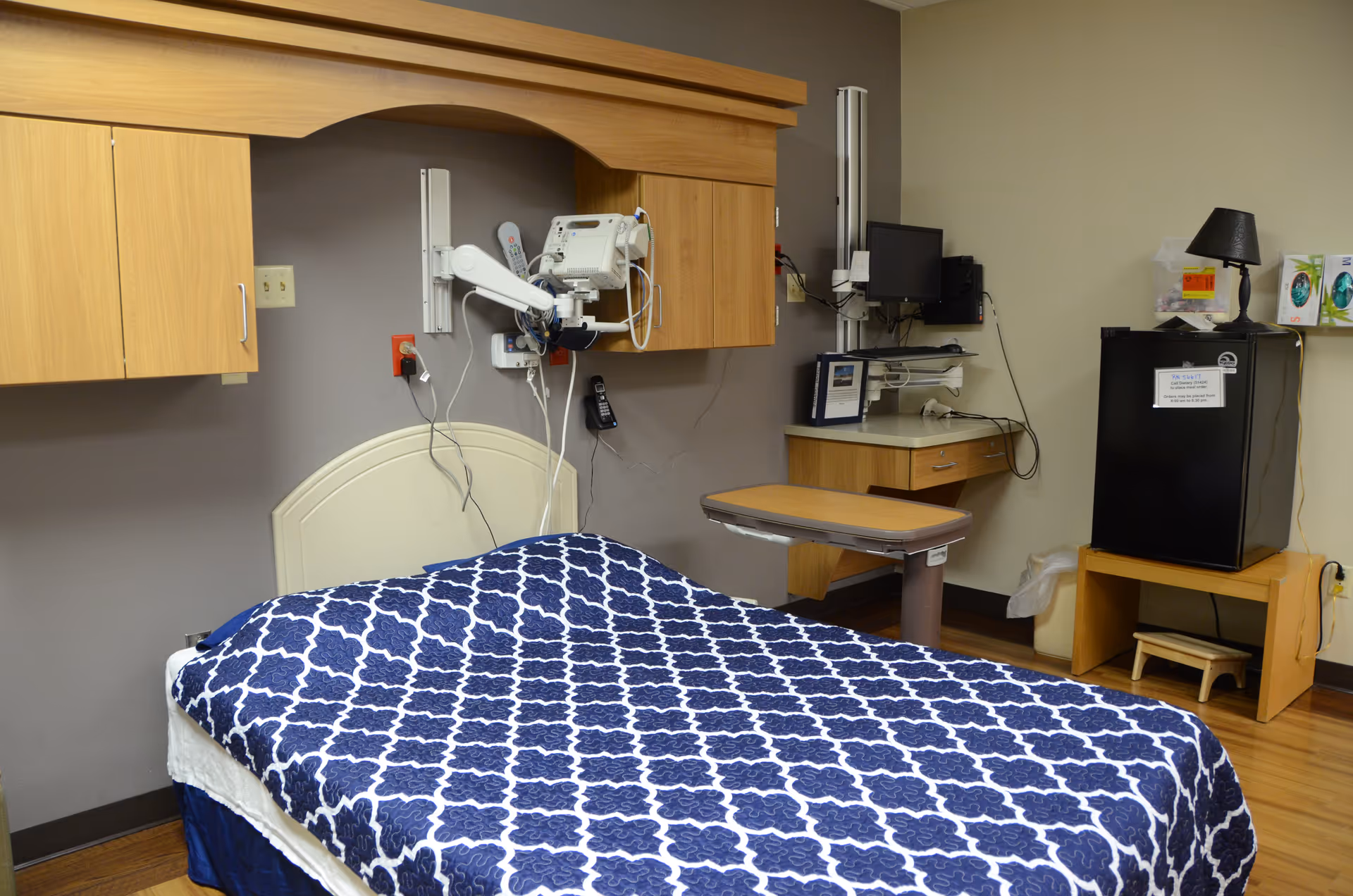 Hospital-style patient room with bed, medical equipment, cabinetry, and a small fridge.
