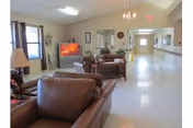 A spacious lounge in a nursing home with brown leather seating and a TV.