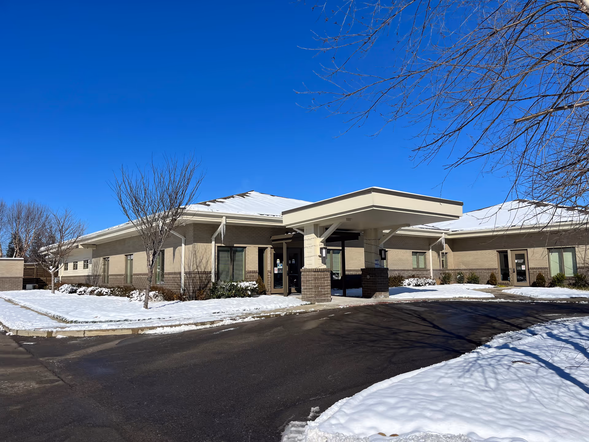 Front exterior of a beige hospice building with a snow-covered driveway.