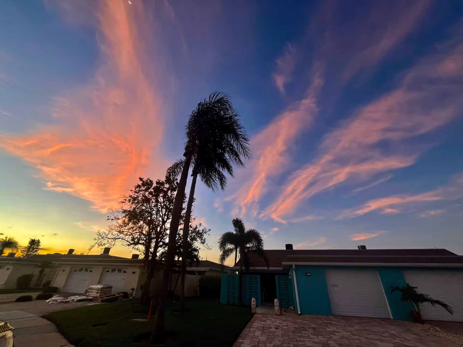 Sunset sky over a row of single-story homes with palm trees and garages.