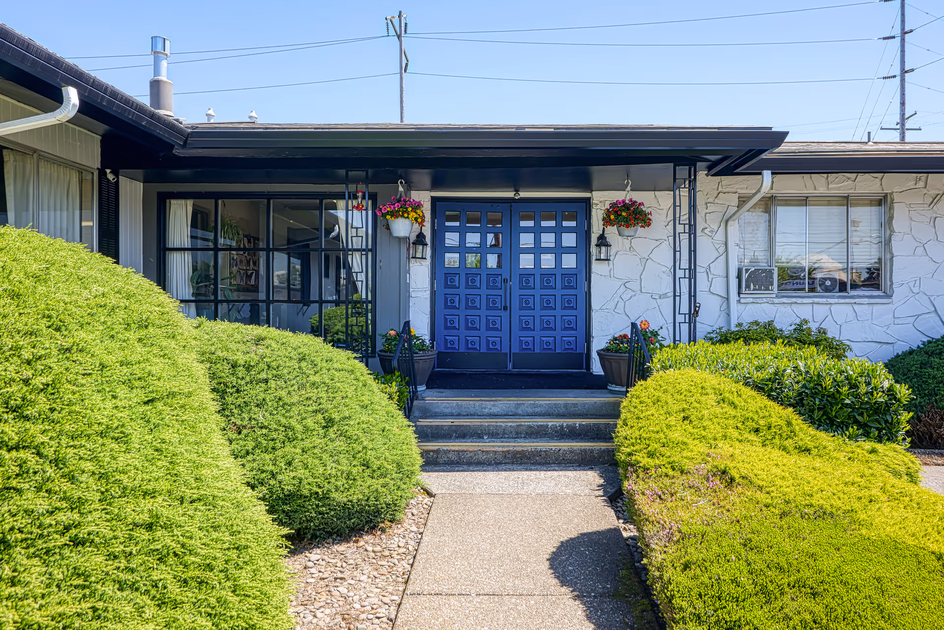 Front entrance of Creekside Rehabilitation and Nursing with blue doors and landscaped shrubs.