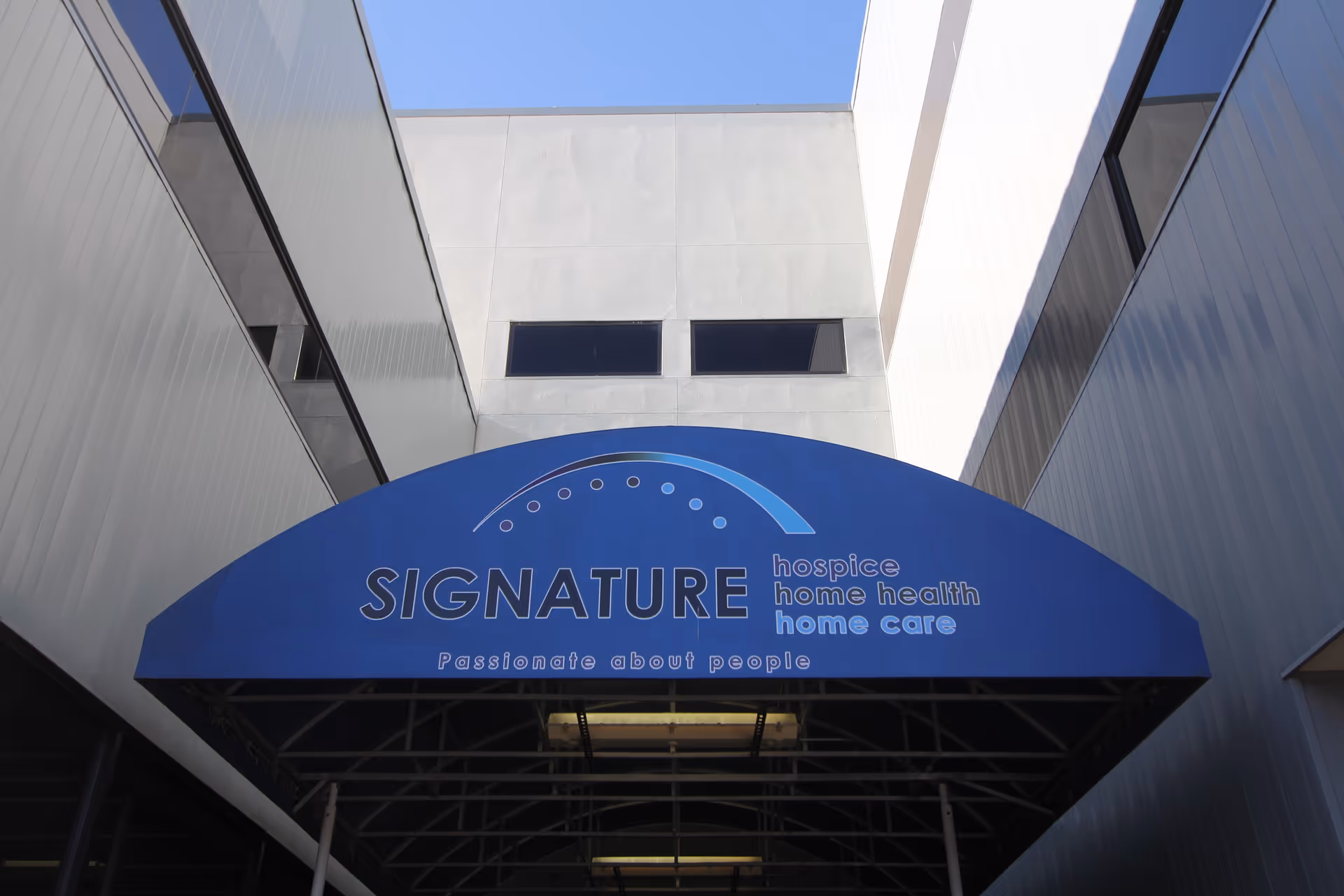 Blue curved sign reading SIGNATURE hospice at a modern building entrance canopy