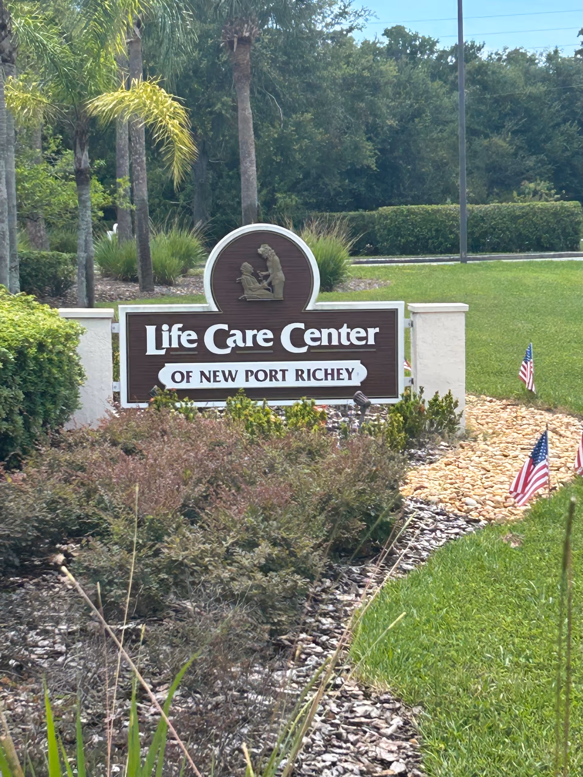Outdoor sign for Life Care Center of New Port Richey amid palm trees.