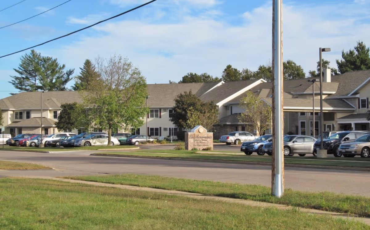 Street view of a senior living facility front with parked cars, an entrance sign, and landscaped lawn.