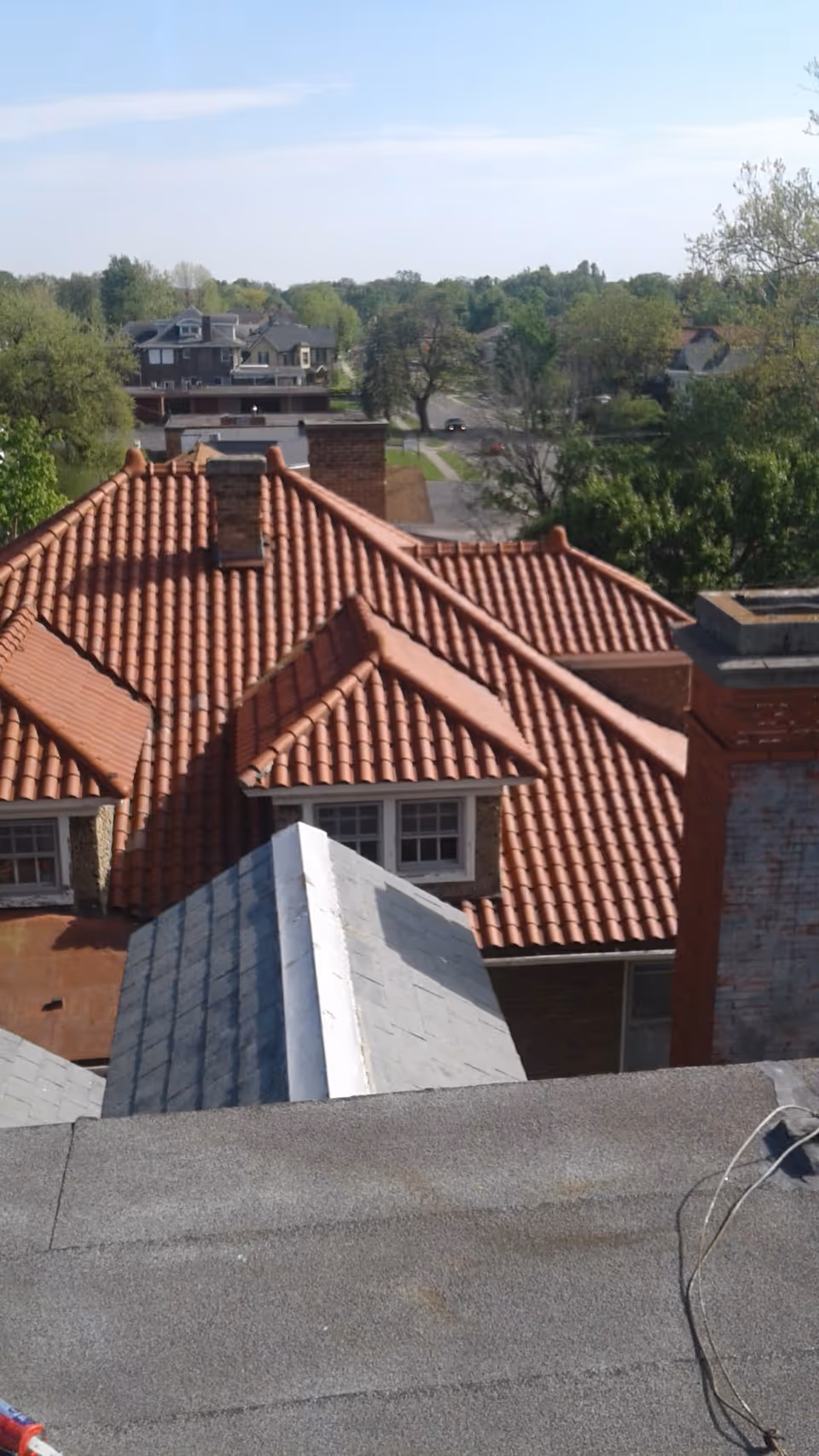 View from above of red clay rooftops and surrounding trees in a residential neighborhood.
