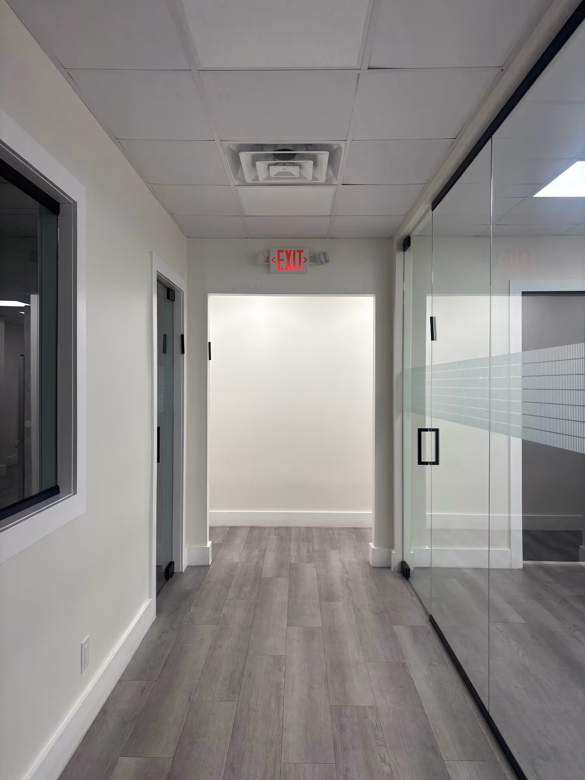 Bright hallway with glass doors, exit sign, and minimalist modern interior.