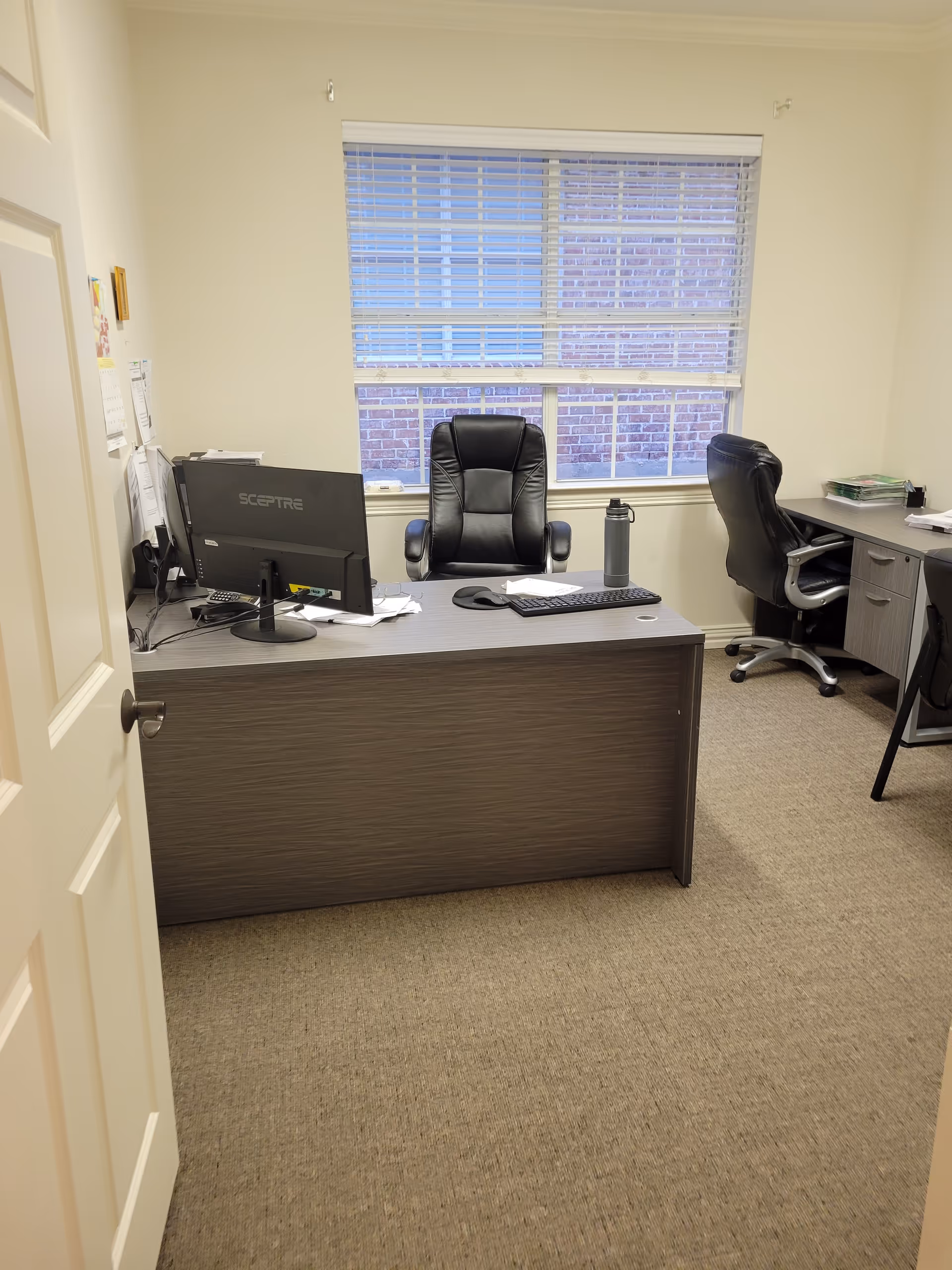 Office desk with computer, keyboard, and chair in a small reception area by a window