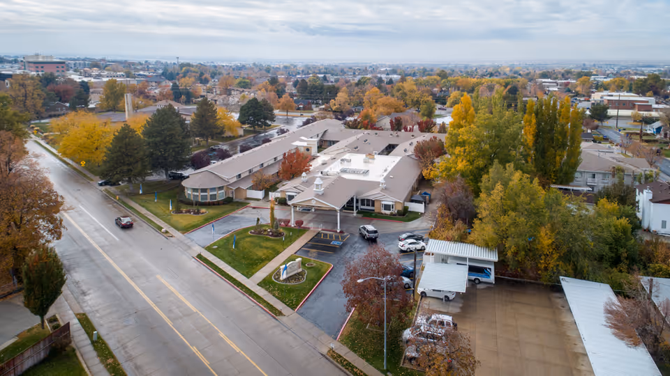 Aerial view of a single-story assisted living facility with an entrance canopy, parking lot, and surrounding autumn trees.