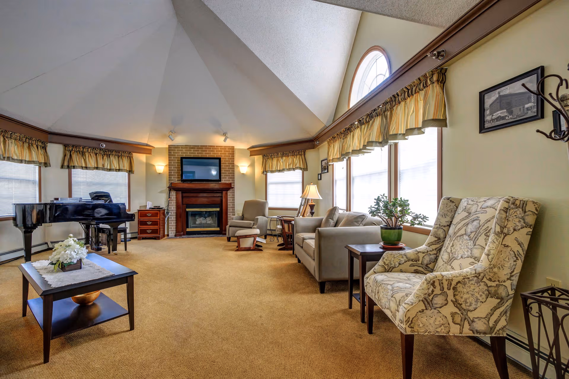 Cozy senior living lounge with fireplace, piano, chairs, and large windows.