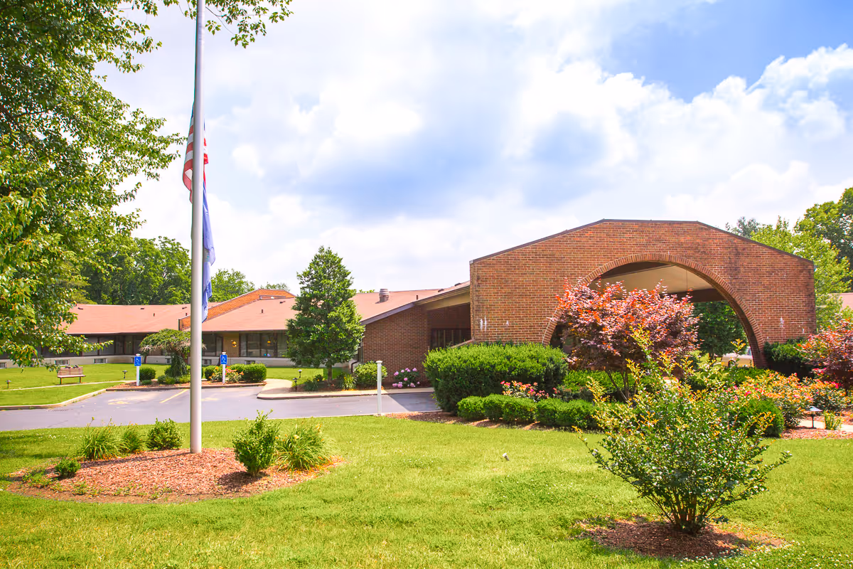 Front exterior of a brick rehab and wellness center with an arched entrance, flagpole, and landscaped lawn.