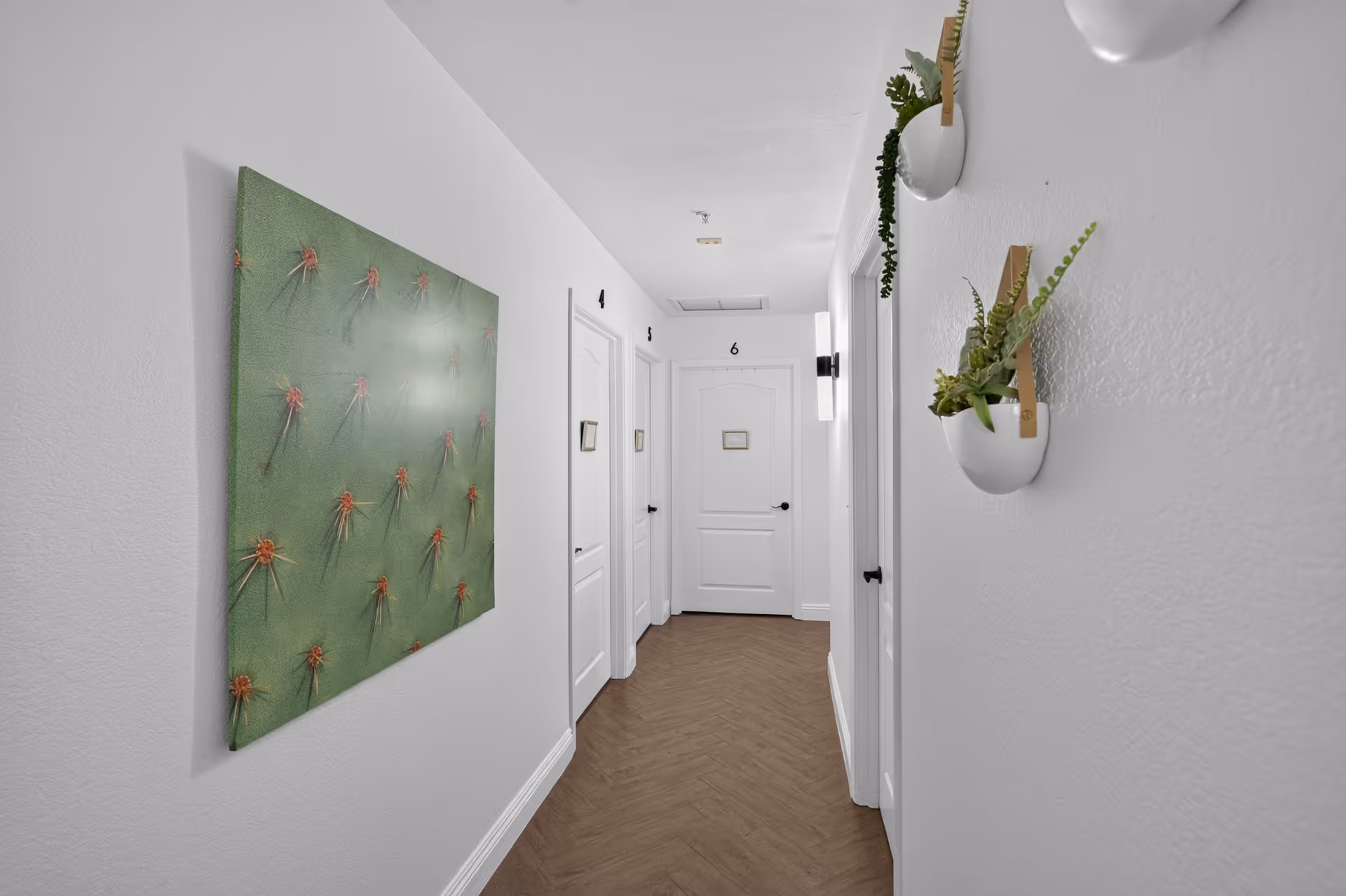 Bright interior hallway with numbered doors, wall art, and white wall-mounted planters.