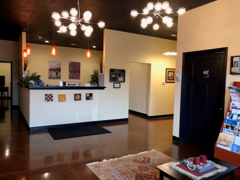 Lobby reception area with a curved desk, pendant lights, and a restroom door.