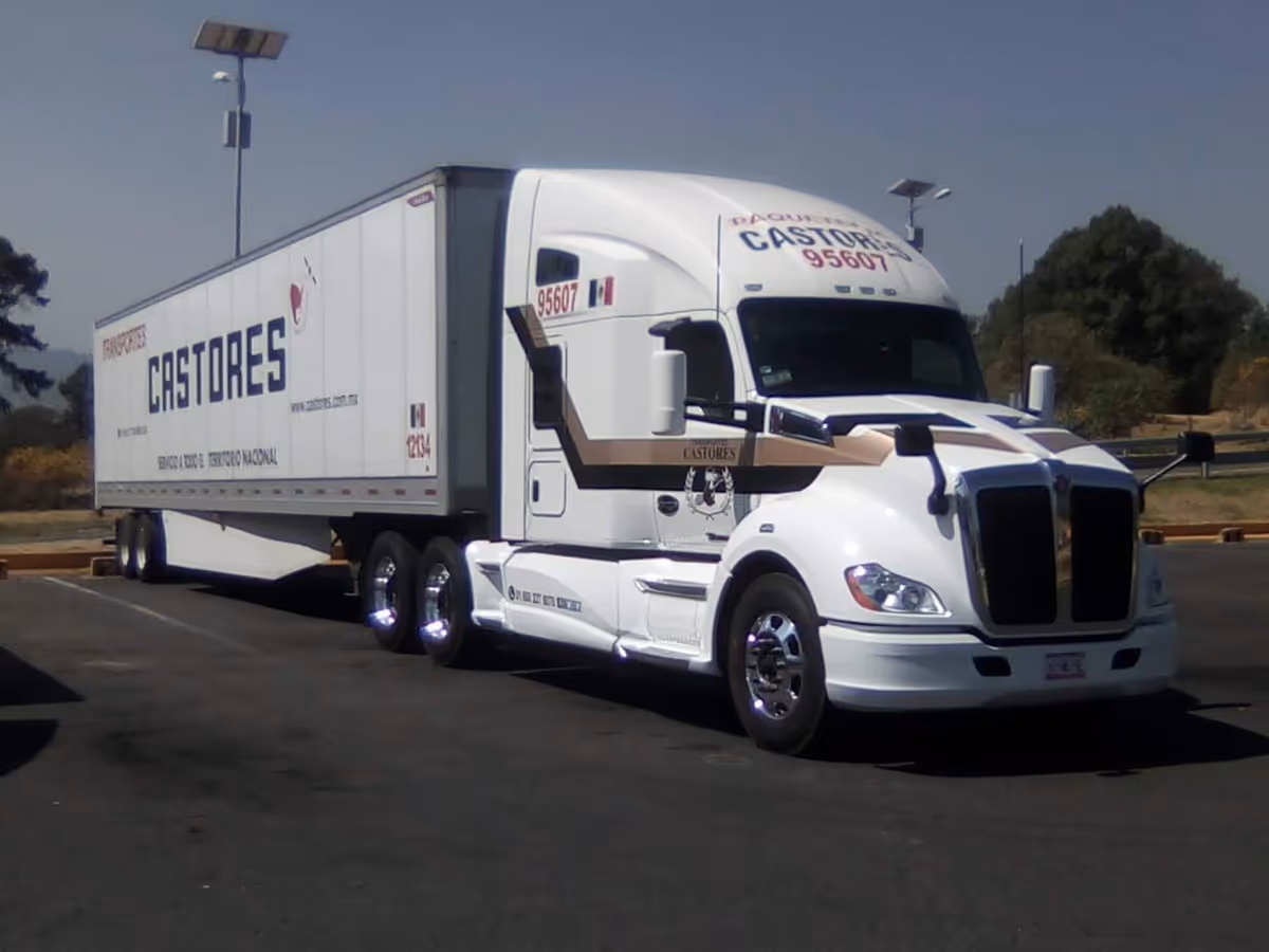 A white tractor-trailer truck with a long trailer parked in an empty parking lot.