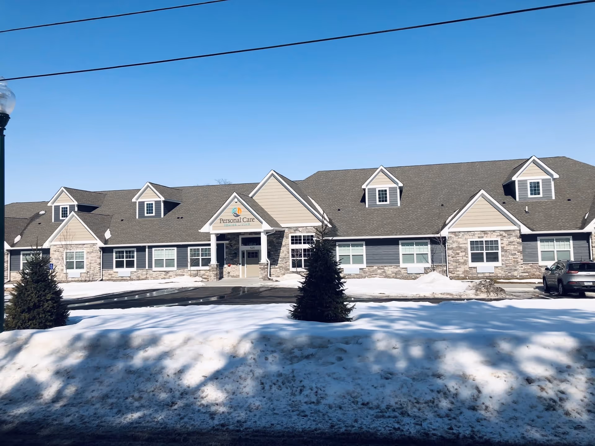 Front exterior of a single-story senior care facility with a 'Personal Care' sign above the central entrance, a parking area, and a snow-covered lawn.