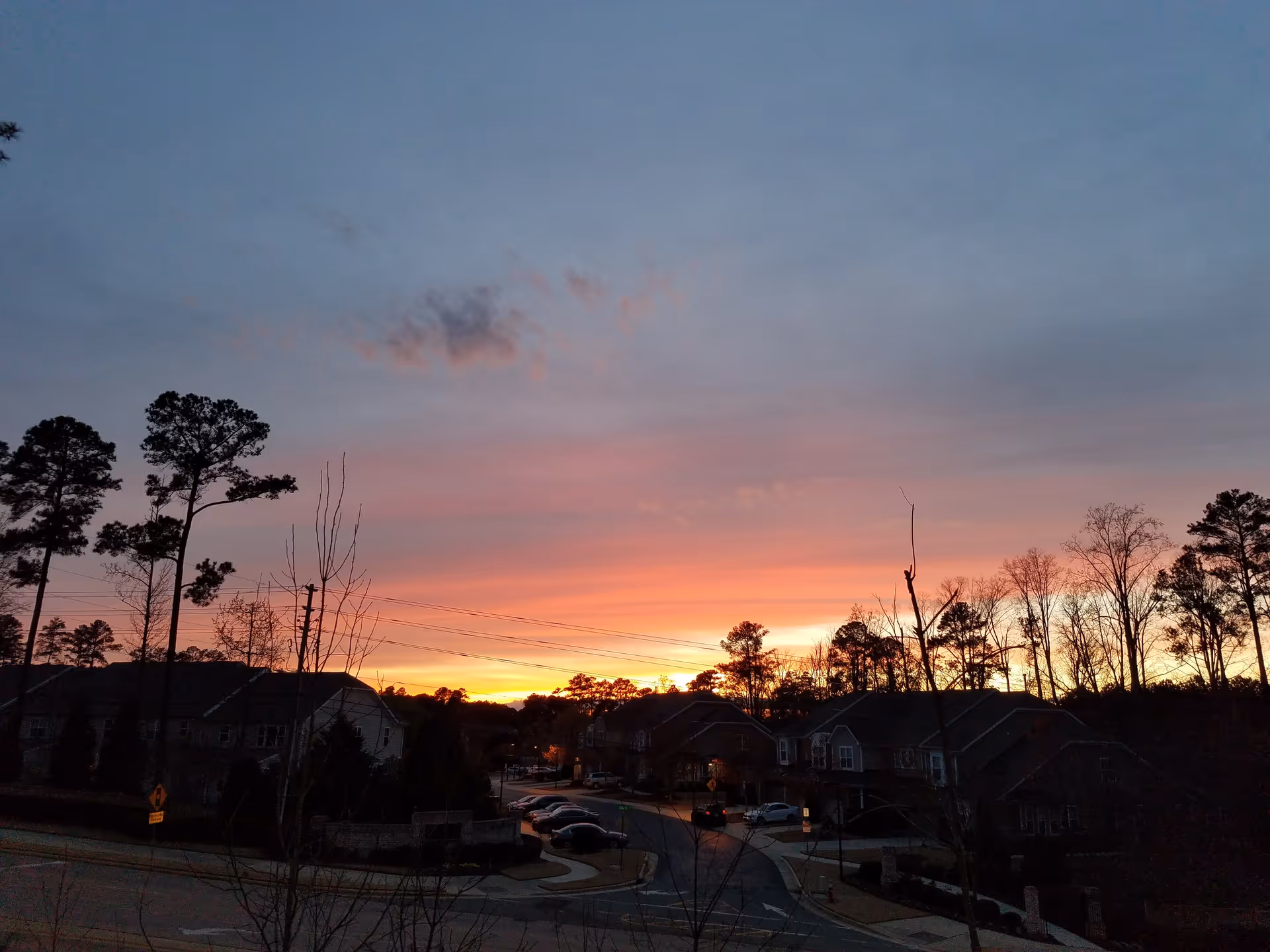Sunset over Willow Creek Senior Living Apartments complex, with leafless trees, cars, and a curved street.