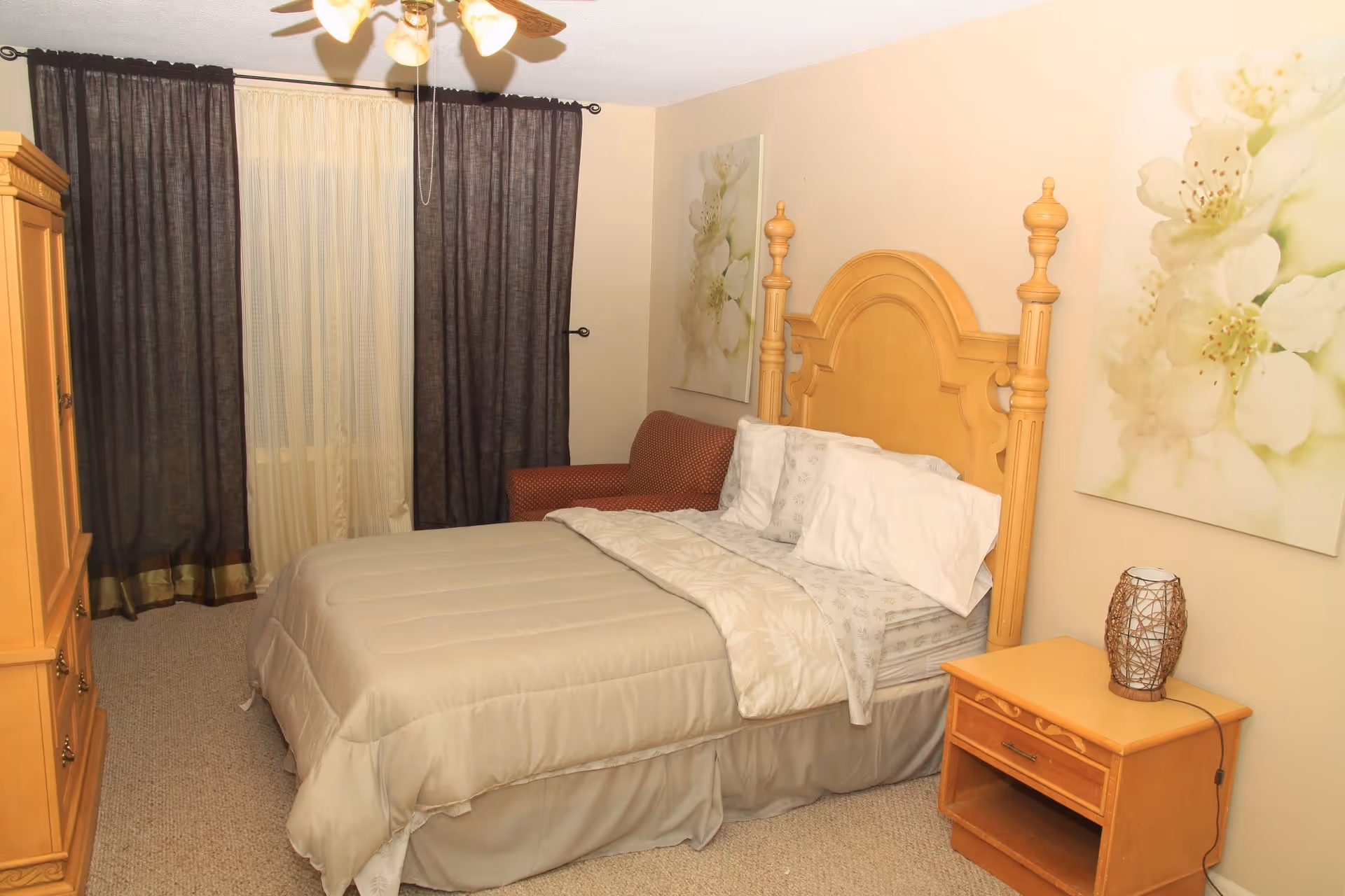 A furnished senior living facility bedroom featuring a wooden bed, nightstand, dresser, and floral art.