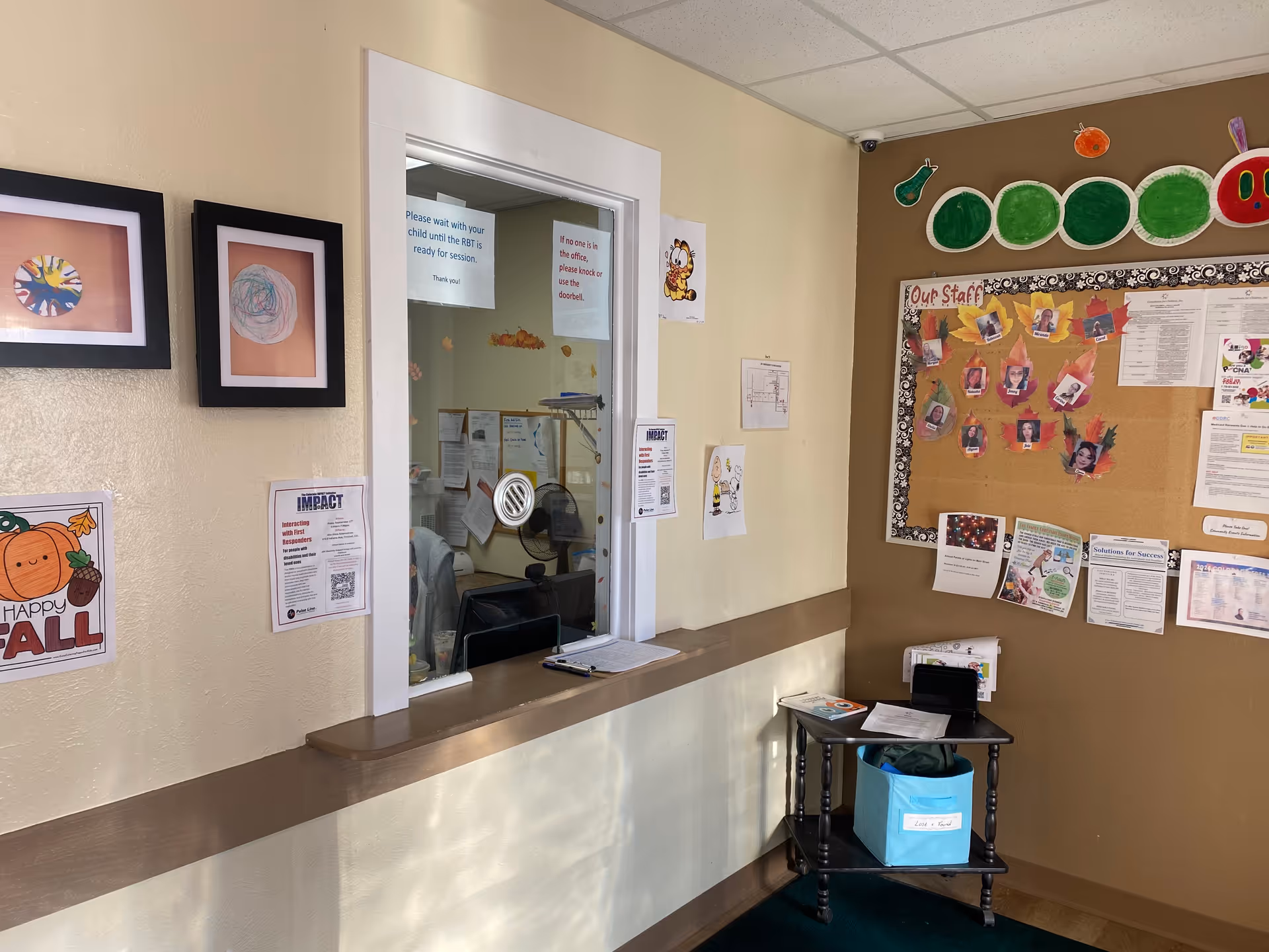 Reception window with a counter, bulletin board, and wall art inside a senior facility.