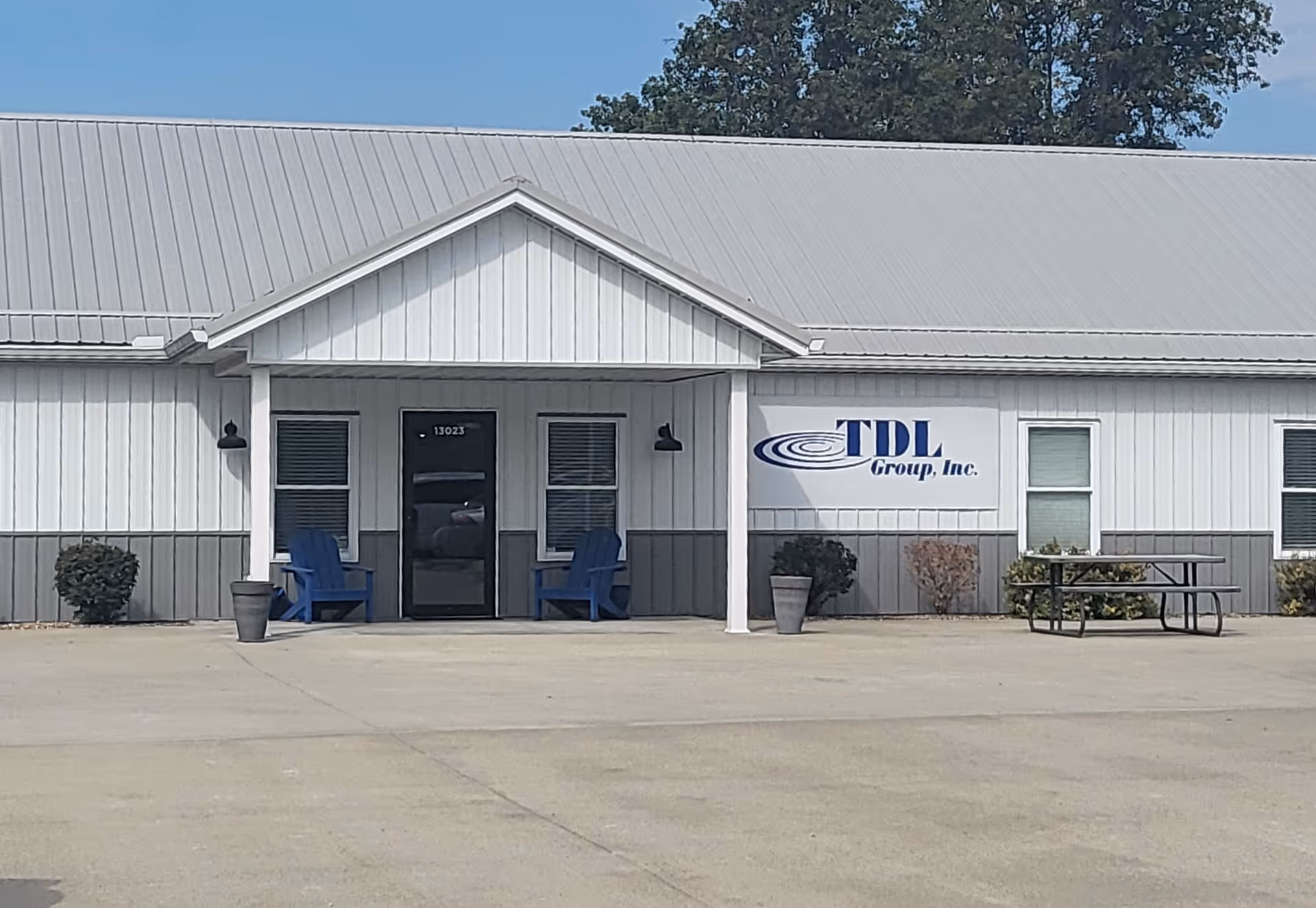 Exterior view of TDL Group, Inc. building with blue chairs and a picnic table.