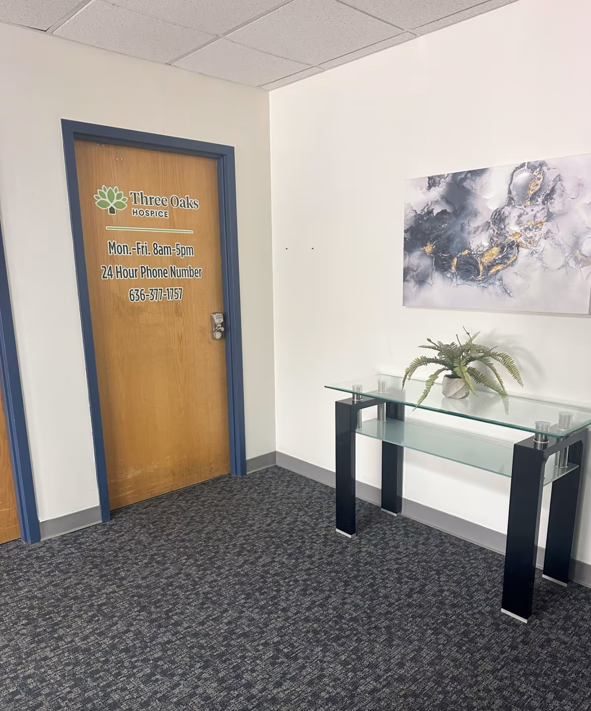 Interior hallway with a wooden door labeled Three Oaks Hospice and a glass console table.