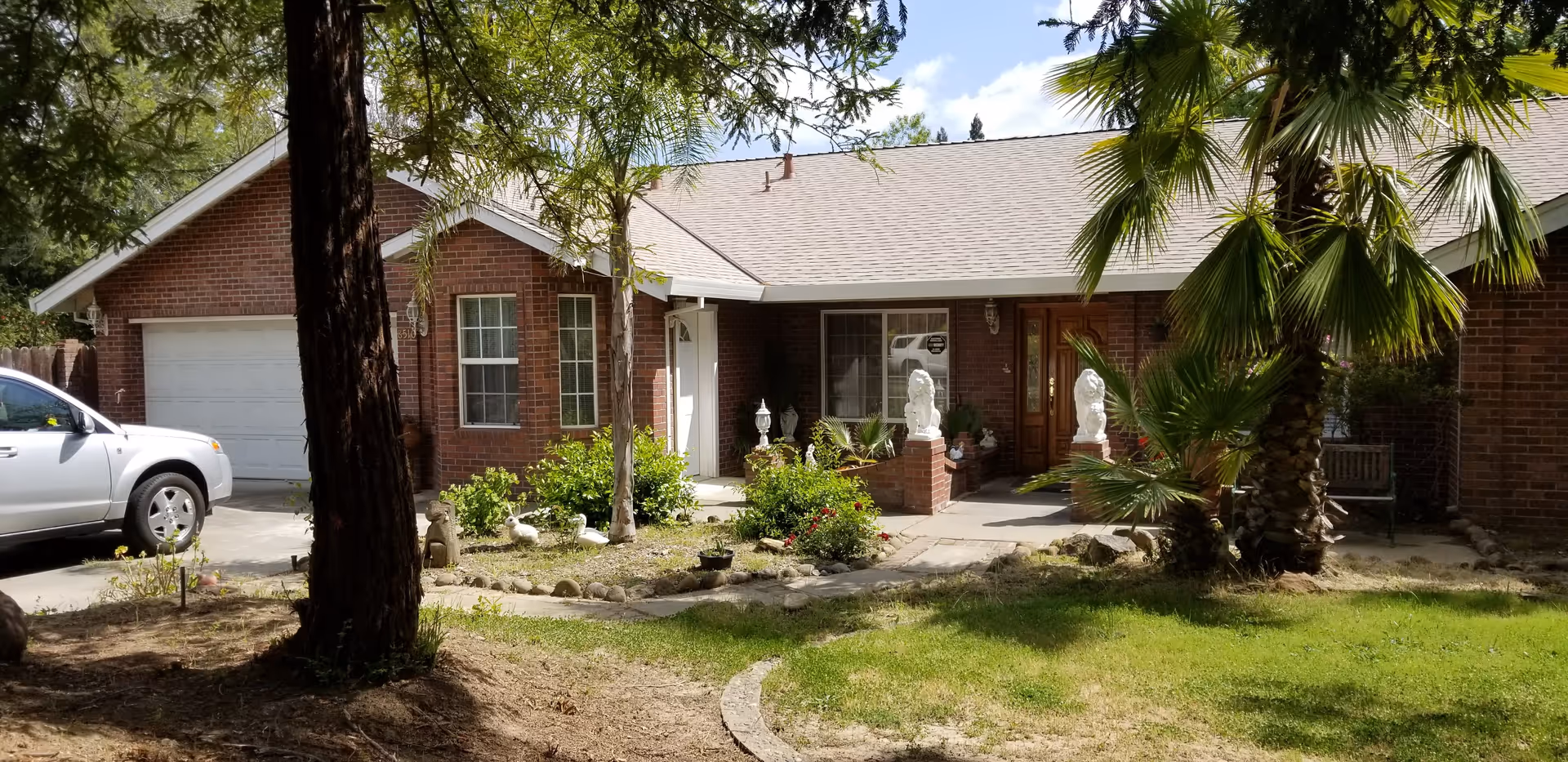 Brick single-story villa with a front yard, palm trees, and a parked white car.