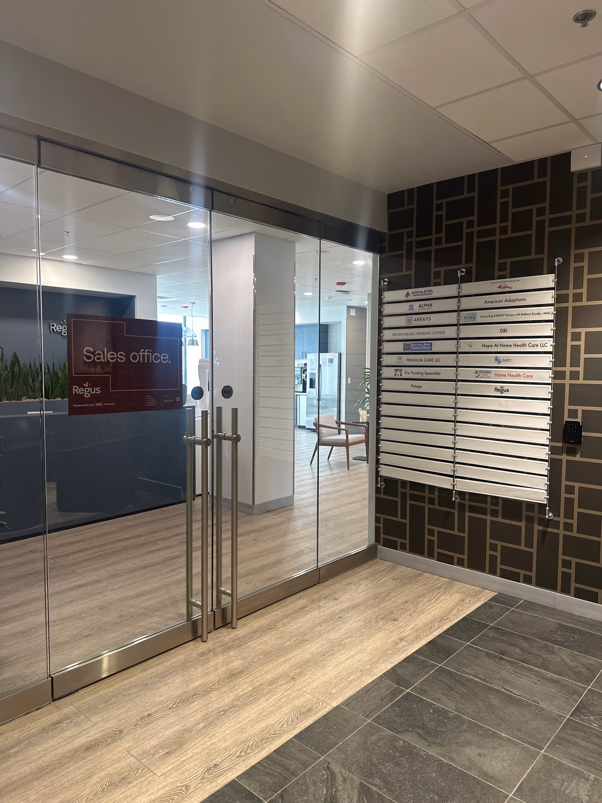 Glass doors open to a modern lobby with a sales office sign and directory board.
