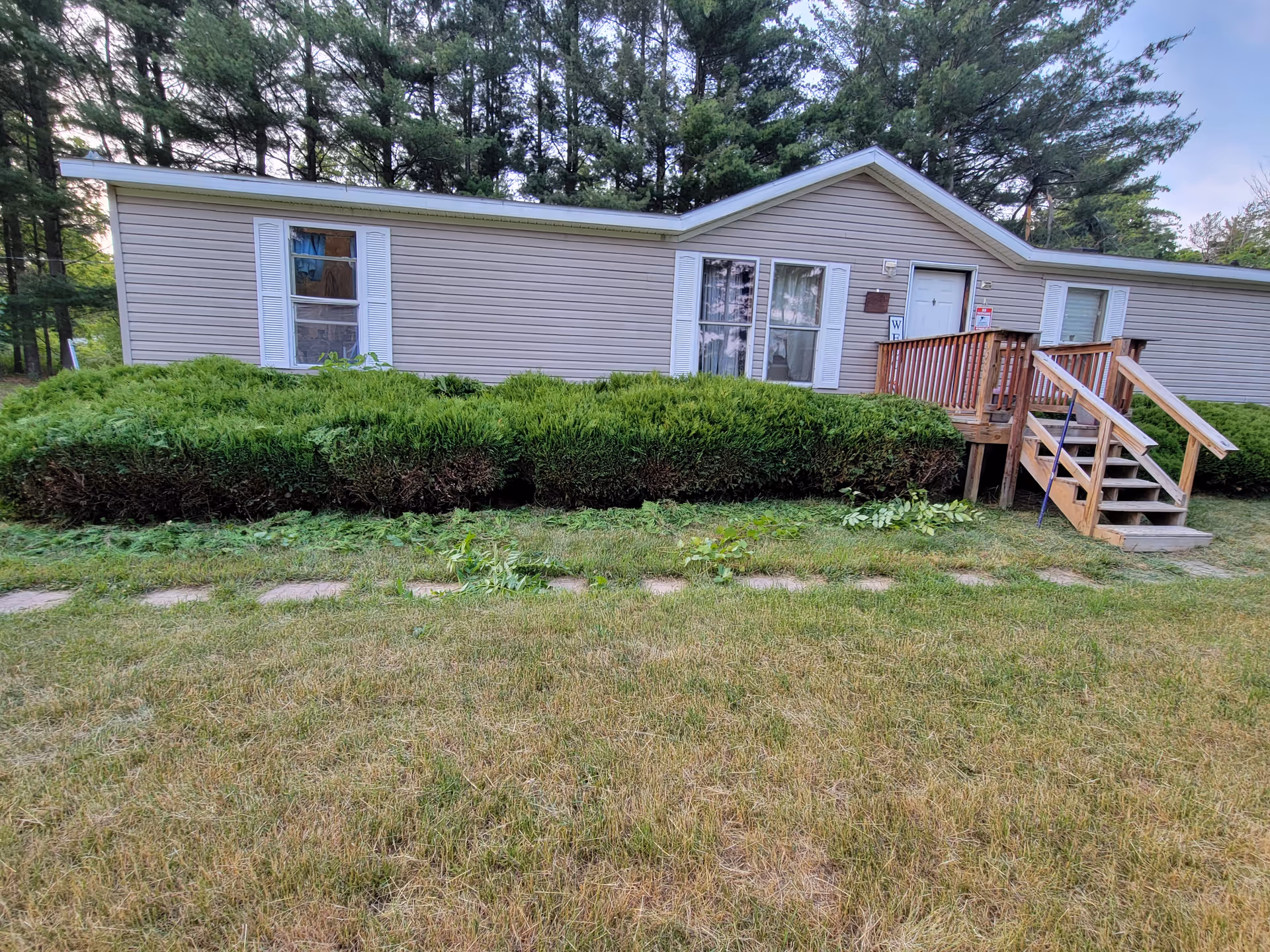 Front exterior of a single-story building with steps, hedges, and trees.
