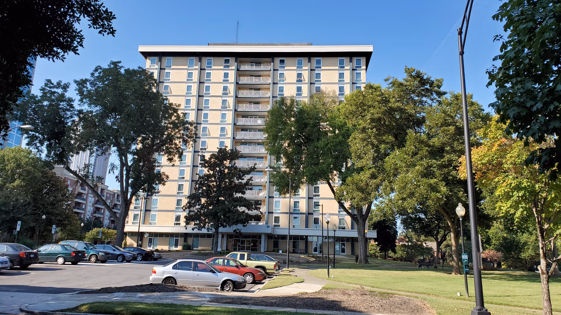 Front view of Charlotte Edwin Towers: a tall beige building with balconies, trees, and parked cars.