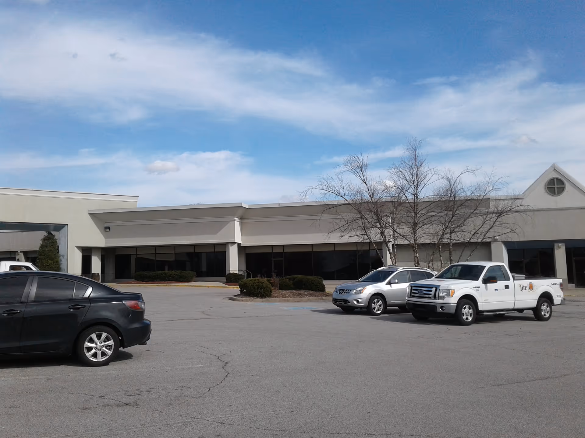 A single-story beige building with large storefront windows and several cars parked in the front lot.