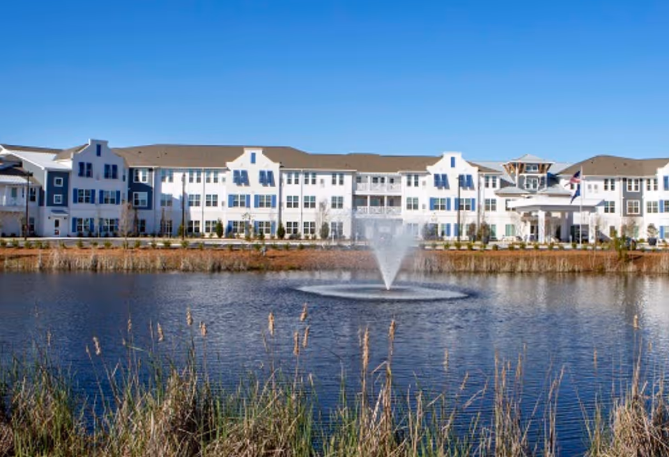 A white multi-story senior living building along a lake with a central fountain.